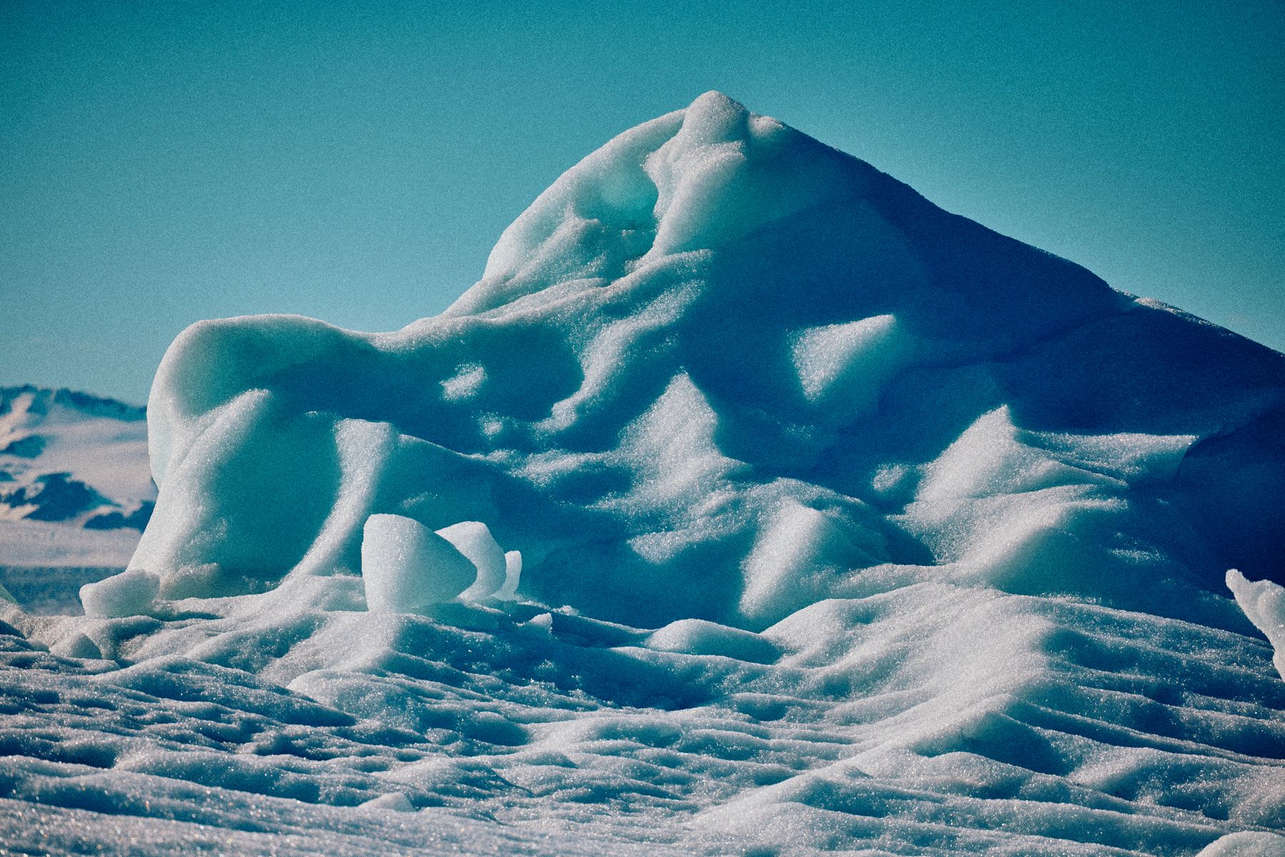 A close-up of a large, sunlit iceberg reveals its granular texture and deep blue shadows under a clear sky.