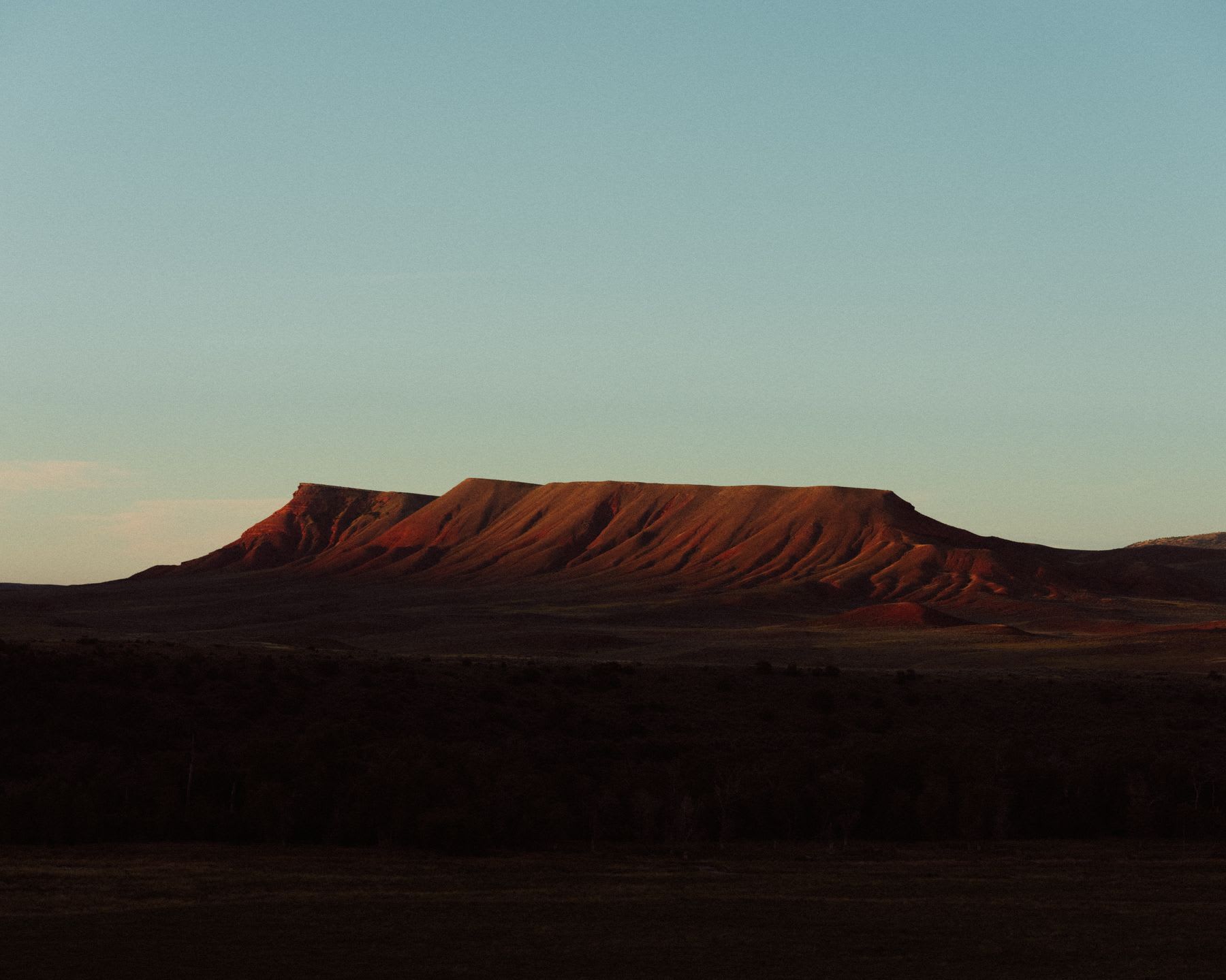 A large flat-topped hill with steep sides under warm sunlight against a clear sky