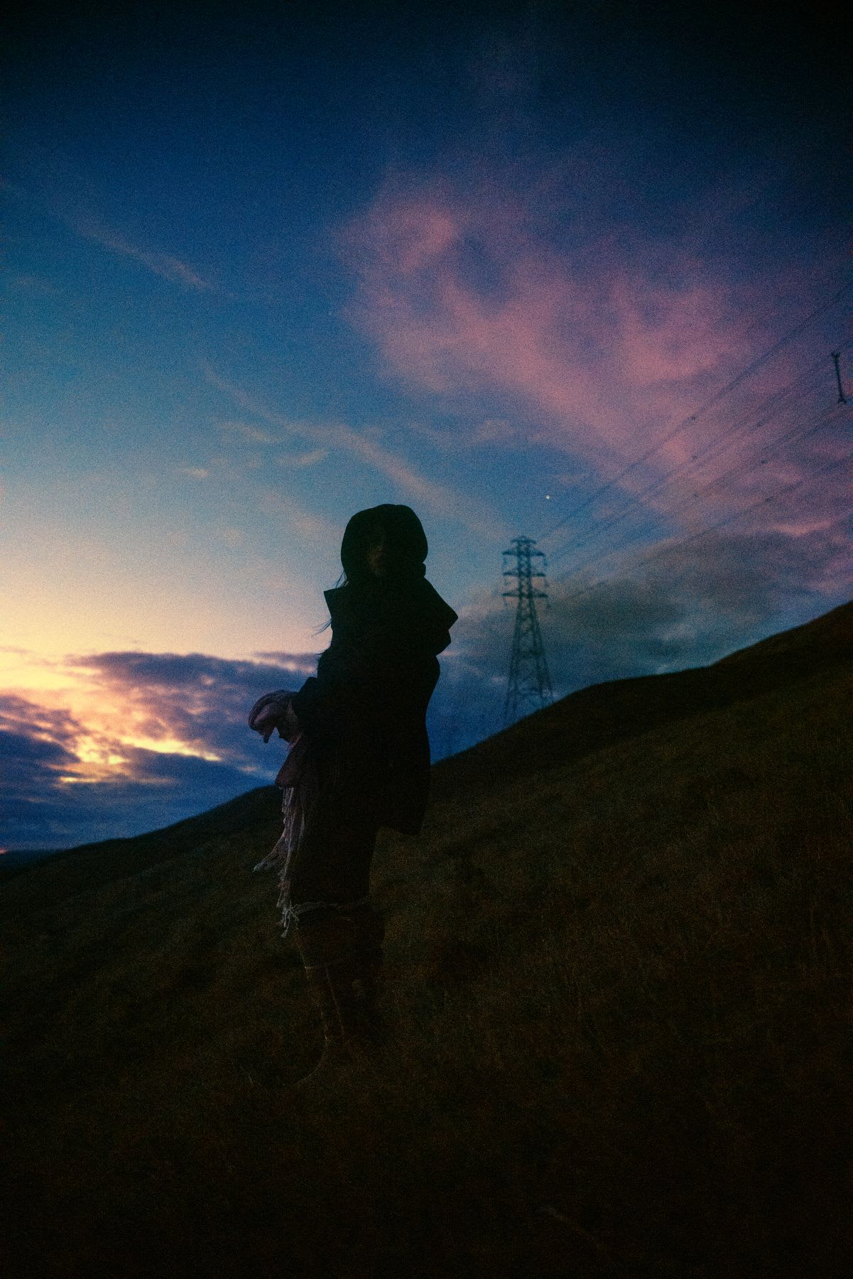 A man in a winter jacket and pants is standing on the side of a mountain near power lines