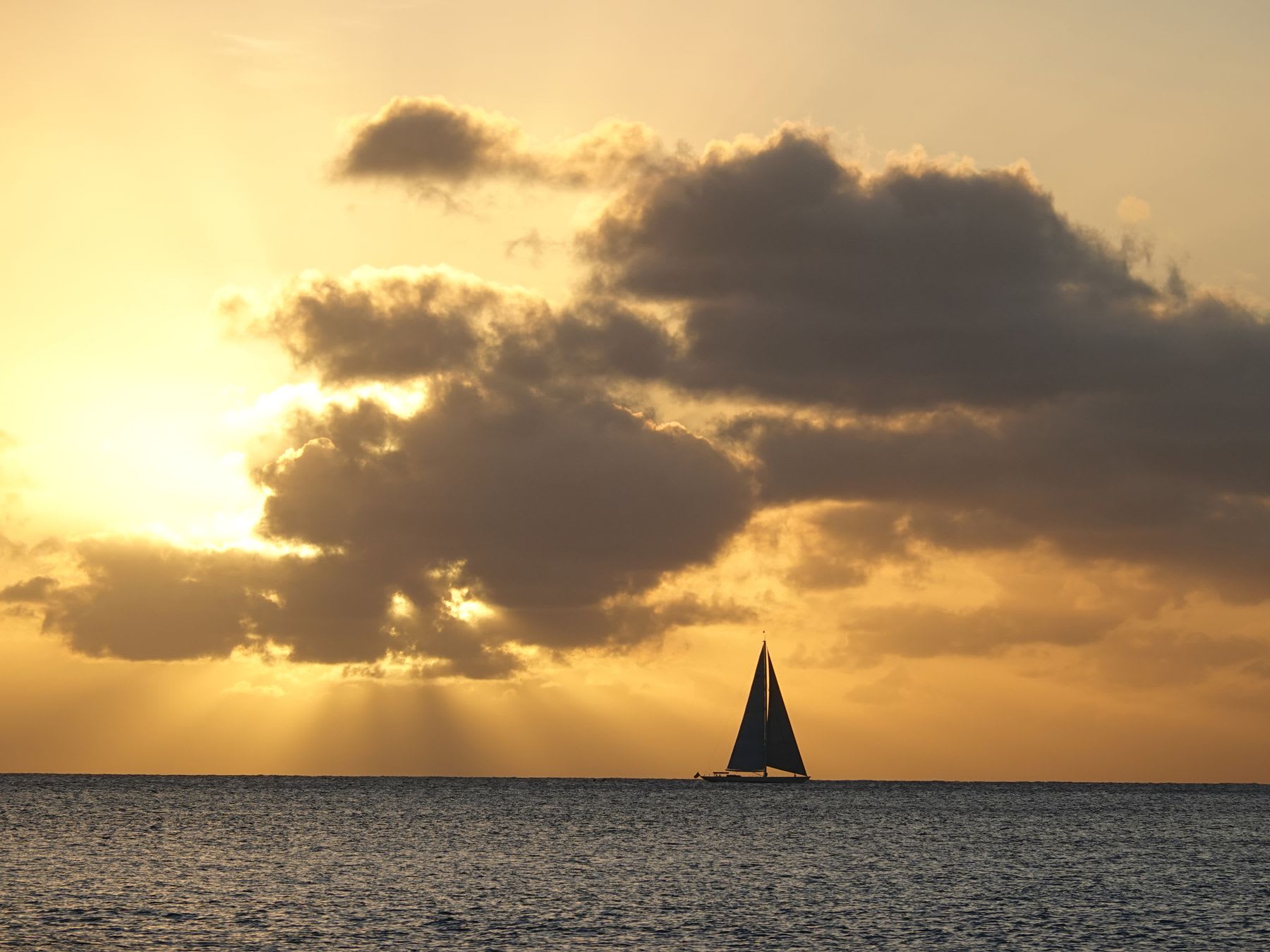 A sailboat sails on the ocean under partly cloudy skies at dusk.