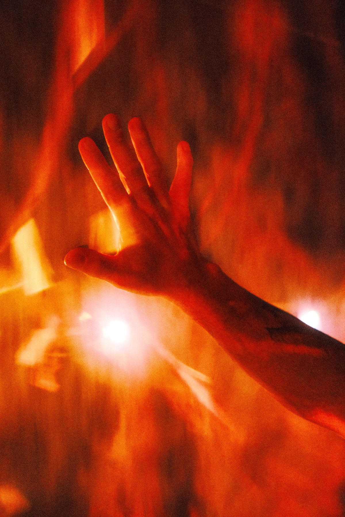 A person's hand is silhouetted against a fiery, glowing orange and red background.