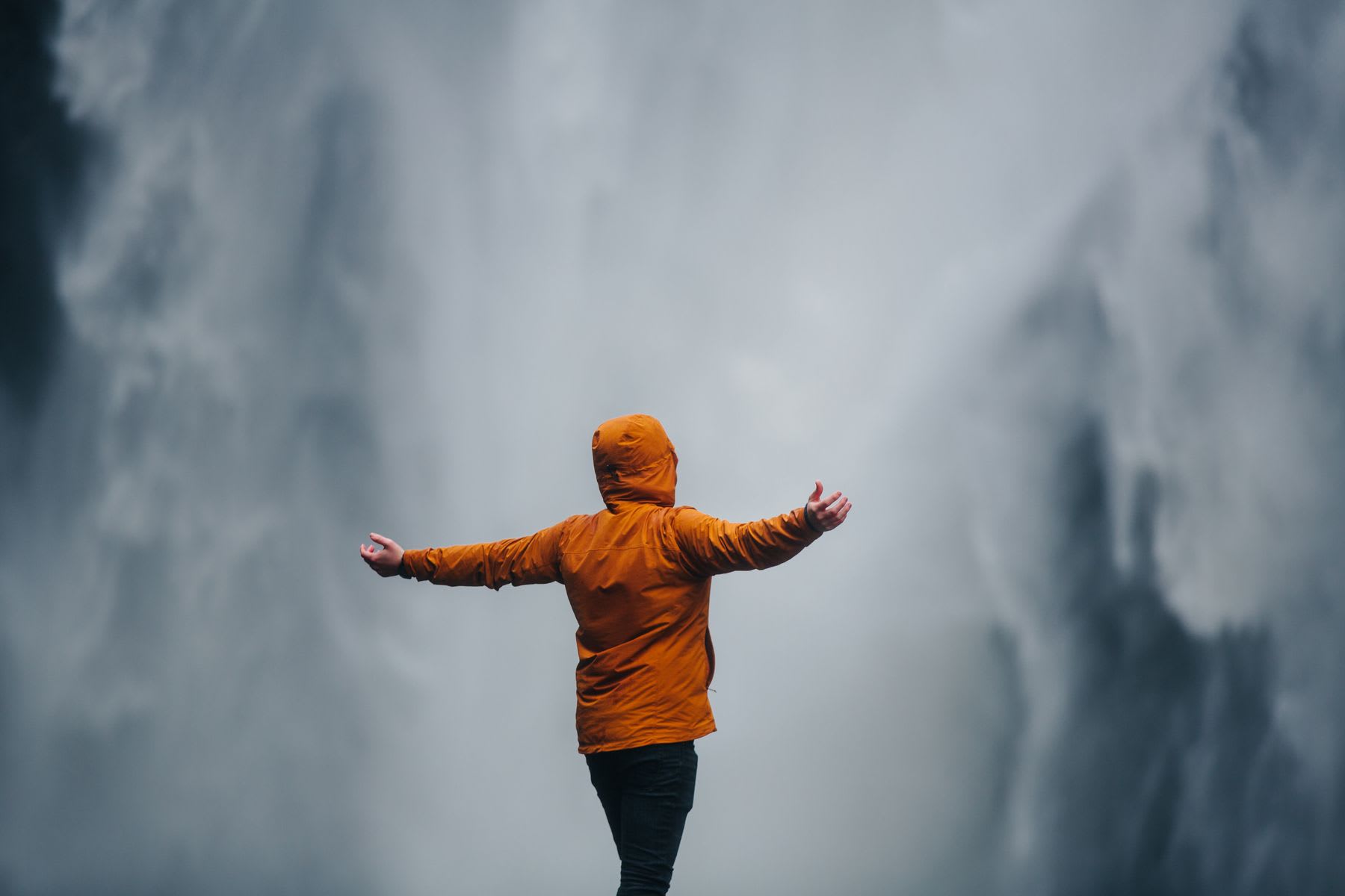 Someone embracing waterfalls while wearing a brown hoodie jacket in an outdoor setting during the day