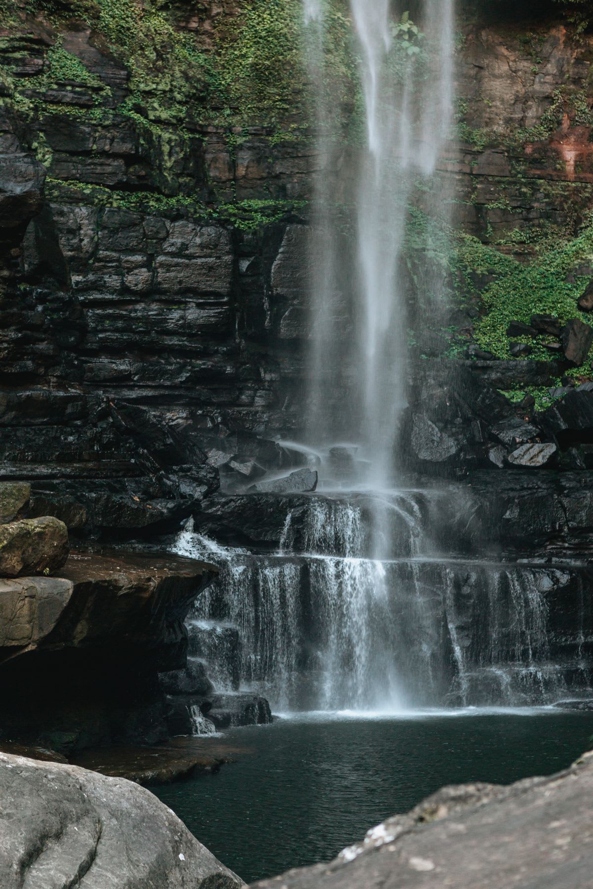 A waterfall cascading down a rocky cliff, with moss-covered stones and vegetation around.