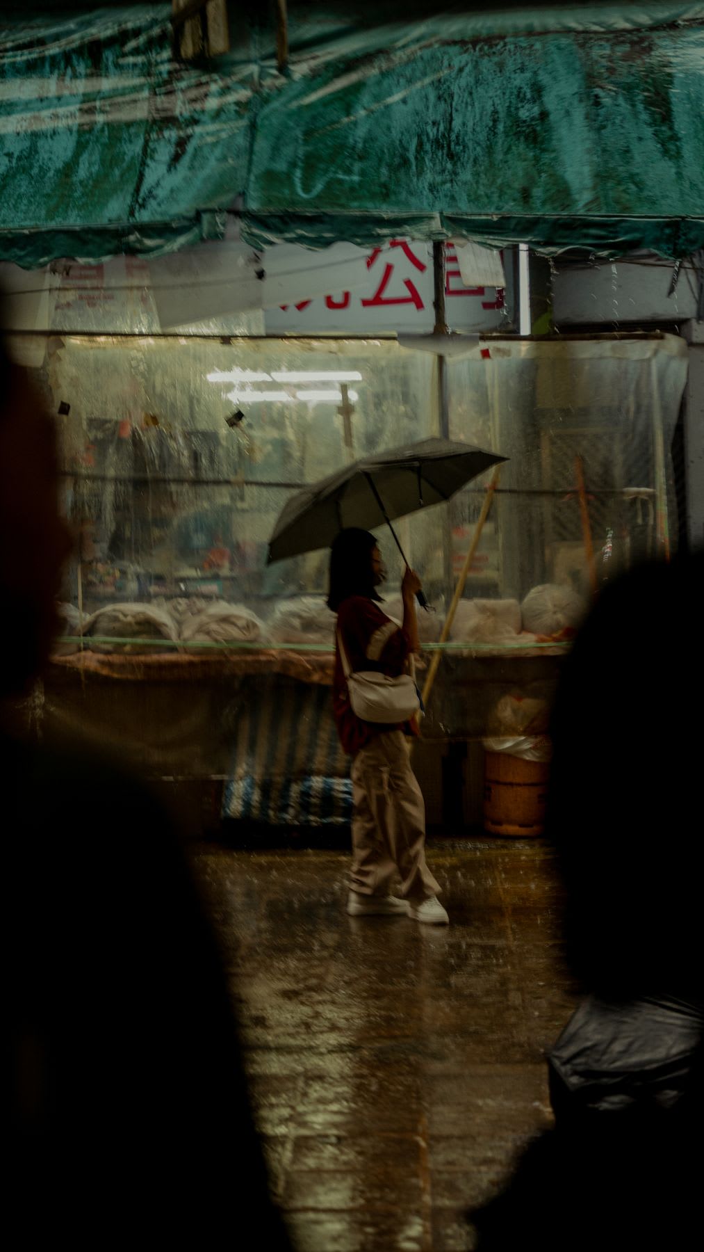 An asian person walks outside a shop holding an umbrella in the rain.