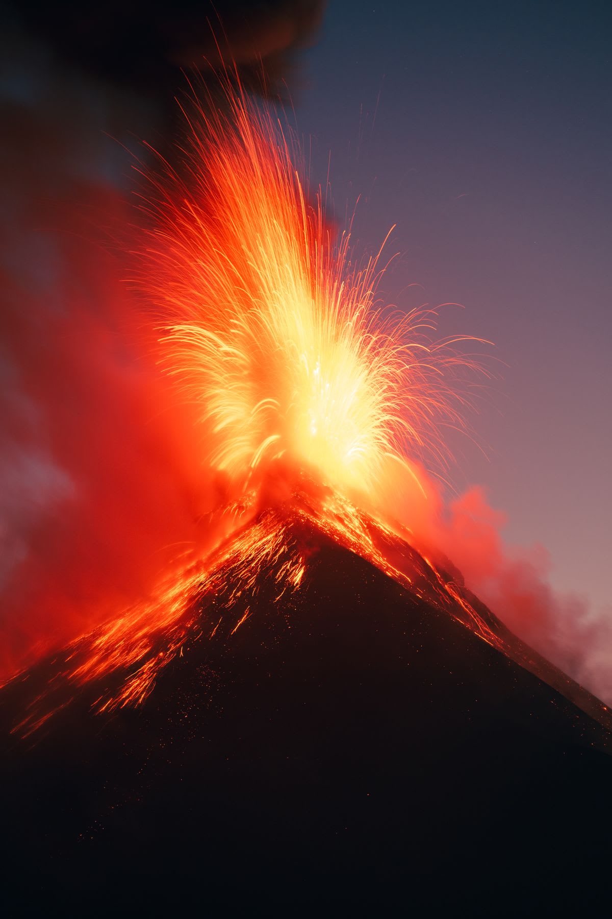 A powerful volcano explodes with fiery lava, illuminating the mountain slopes and the twilight sky.