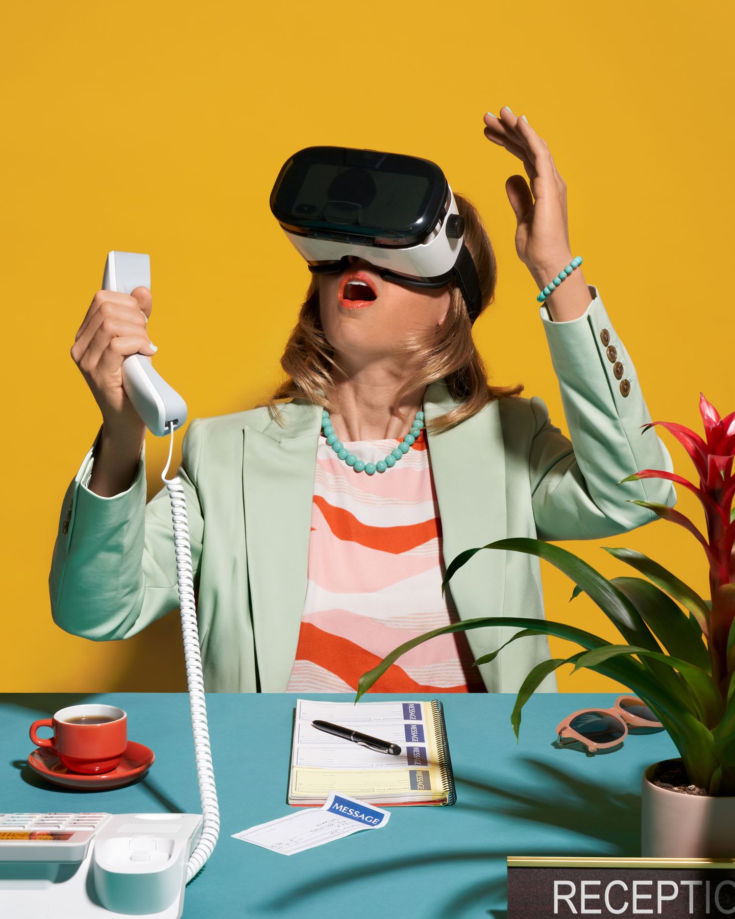 Receptionist wearing a virtual reality headset, holding a phone receiver, and reacting with surprise, seated at a colorful desk with office supplies and a potted plant against a yellow background.