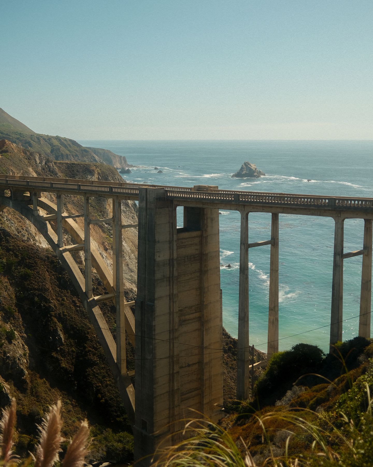 A uniquely structured bridge with a view of the sky blue ocean water.