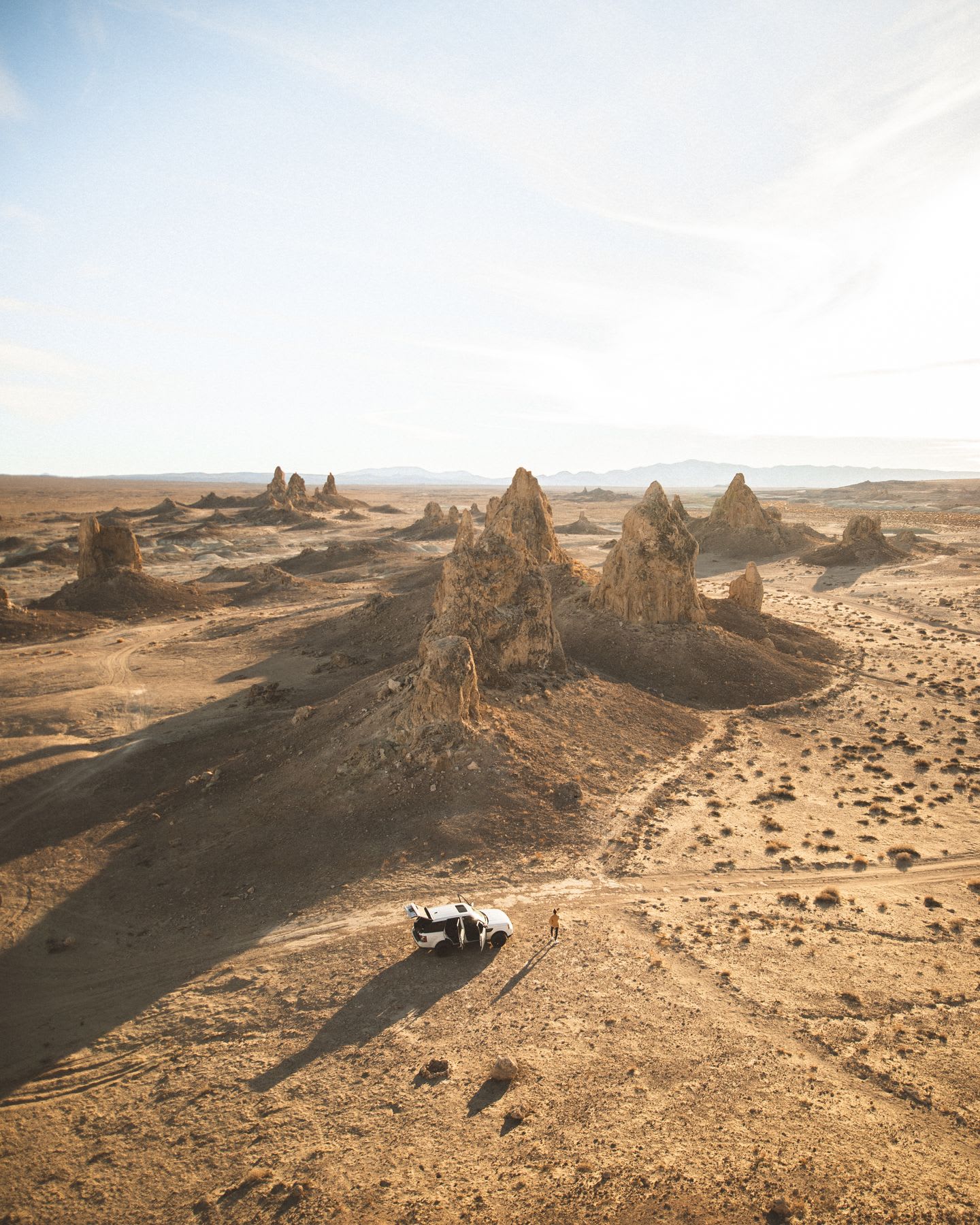 Vehicle and person in a desert landscape with rock formations during daylight.