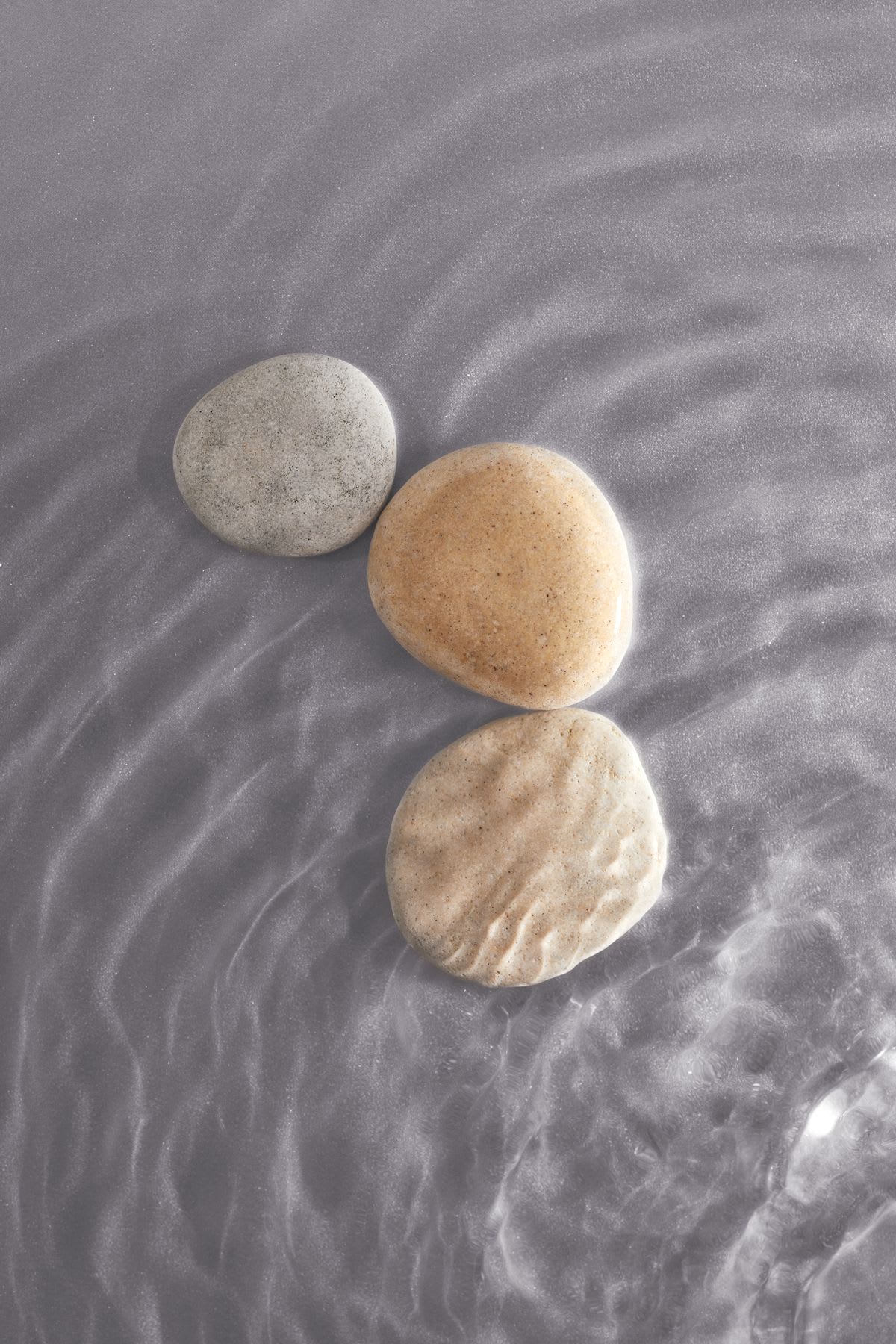 Ripples flow through the translucent water contrasting with three pebbles.