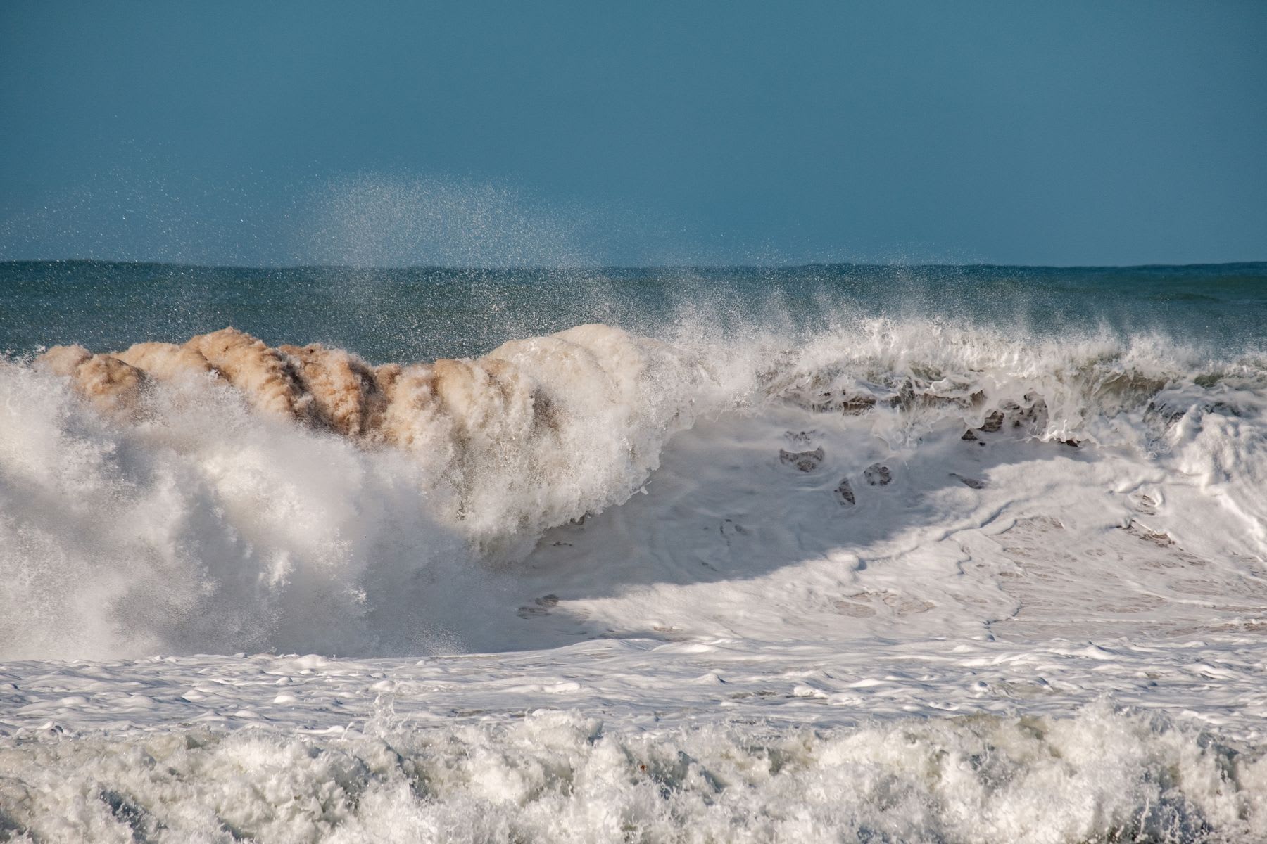 Breaking wave foams while it flows toward the beach on a sunny day.