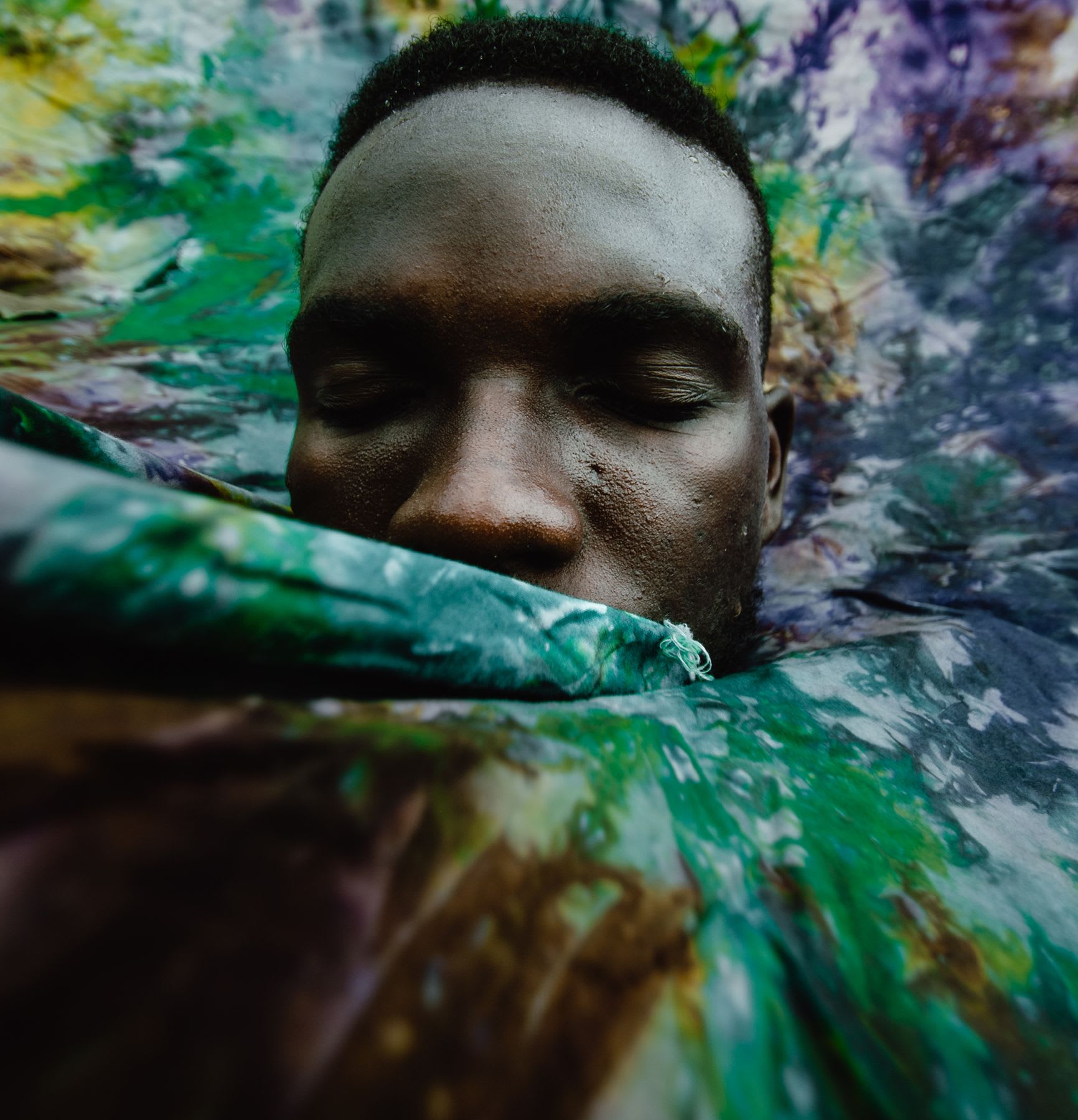 Portrait of a black man with a tie-dyed piece of cloth wrapped around his face.