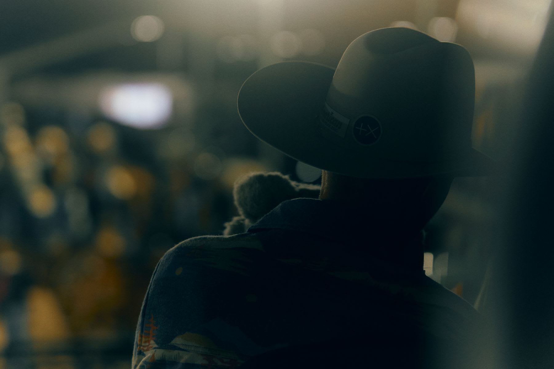 A person wearing a cowboy hat viewed from behind in a dim room