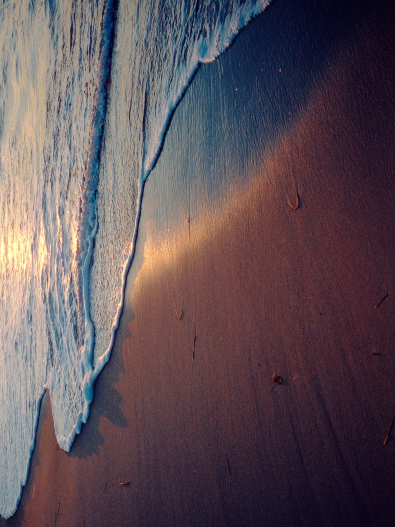Beach at sunset, with the wave gently kissing the sand, creating golden reflections in the water.