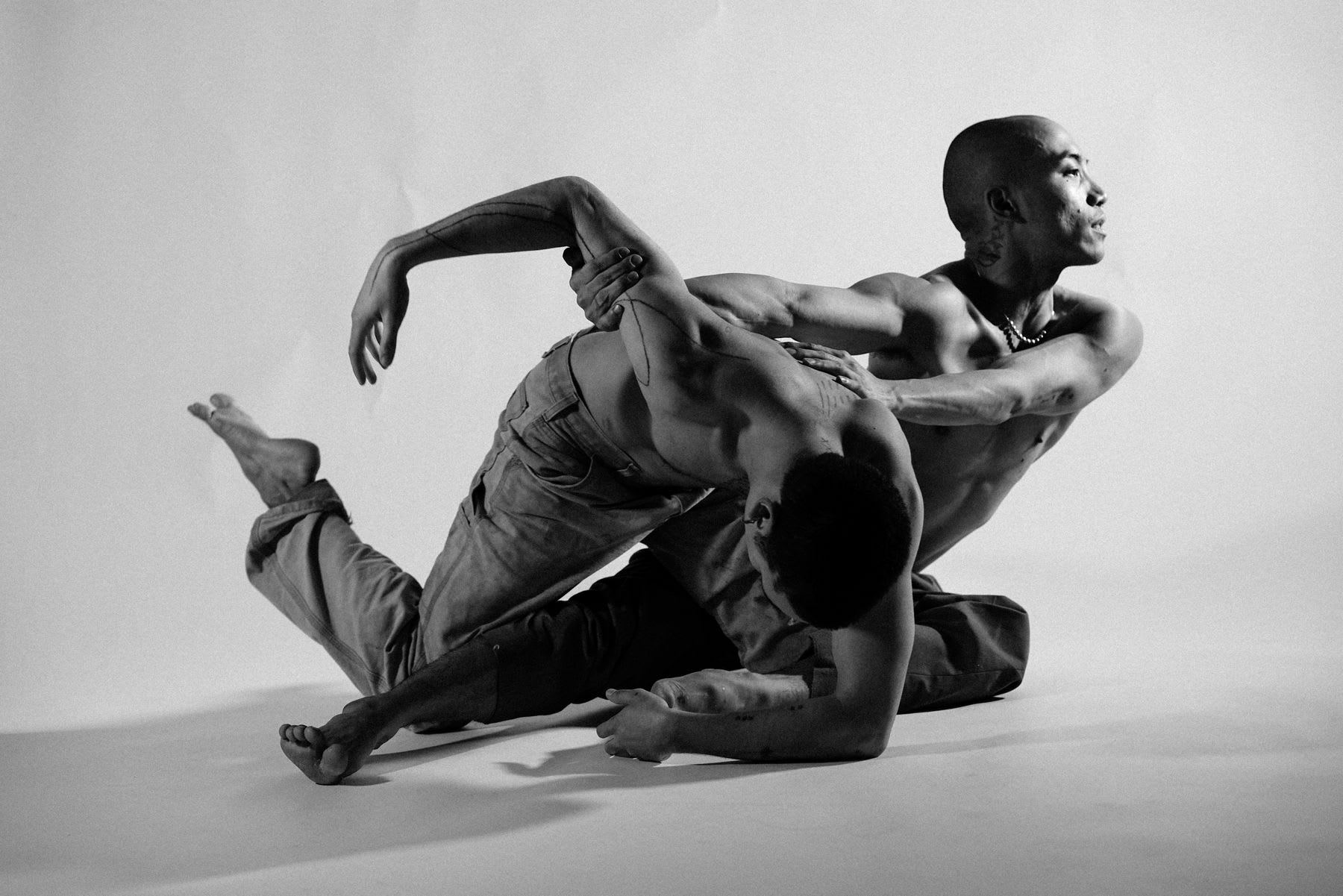 Two male dancers entangled in each other with one pushing to escape