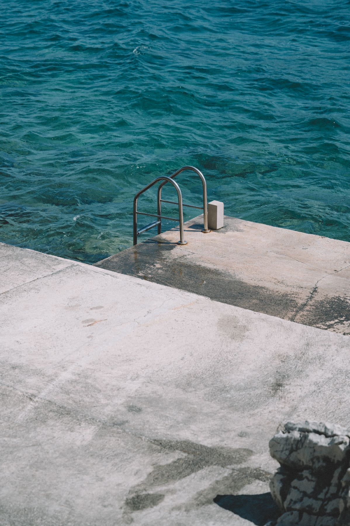 Concrete pier with a metal staircase leading to a clear blue sea.