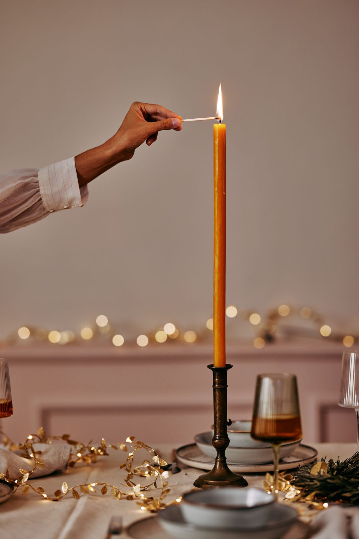 A woman is reaching over the table to light the tall orange candle.