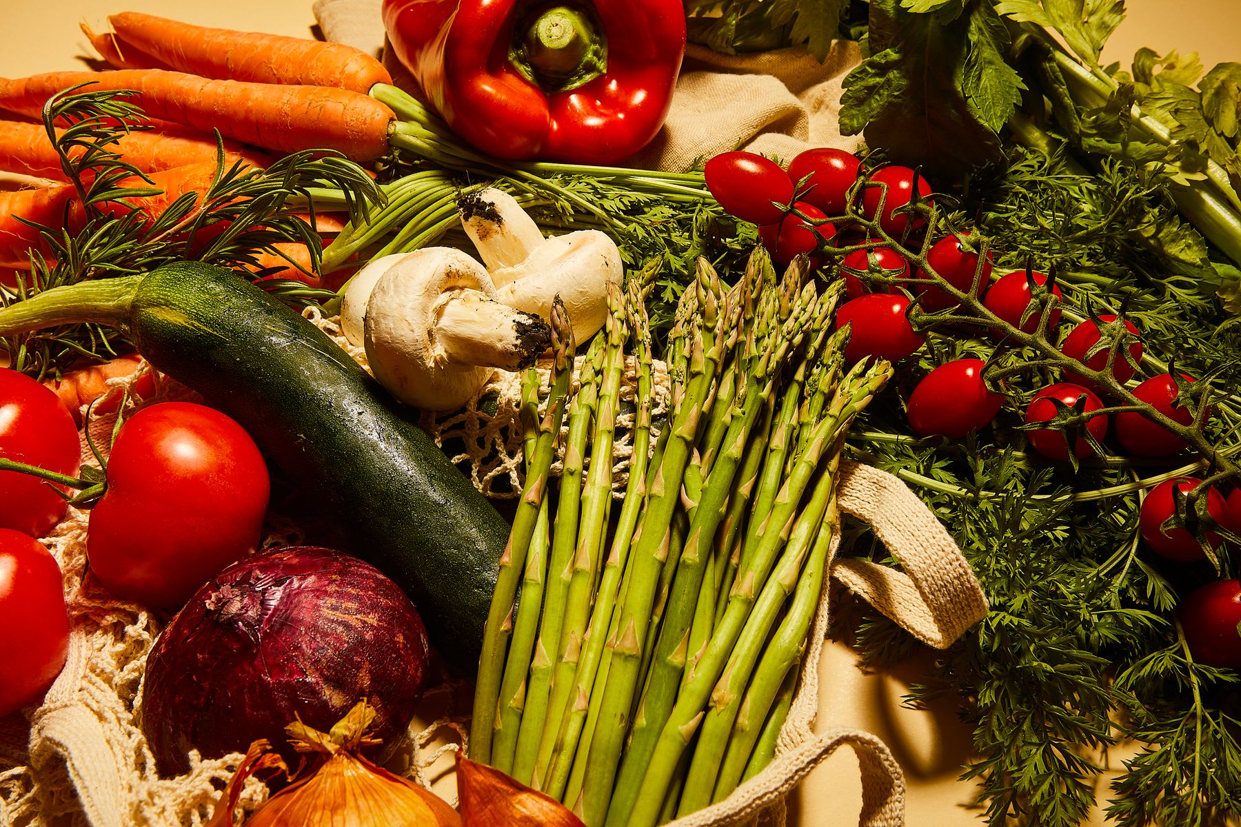 A colorful bounty of fresh market vegetables like asparagus, carrots, tomatoes, and bell peppers are arranged on a rustic surface.