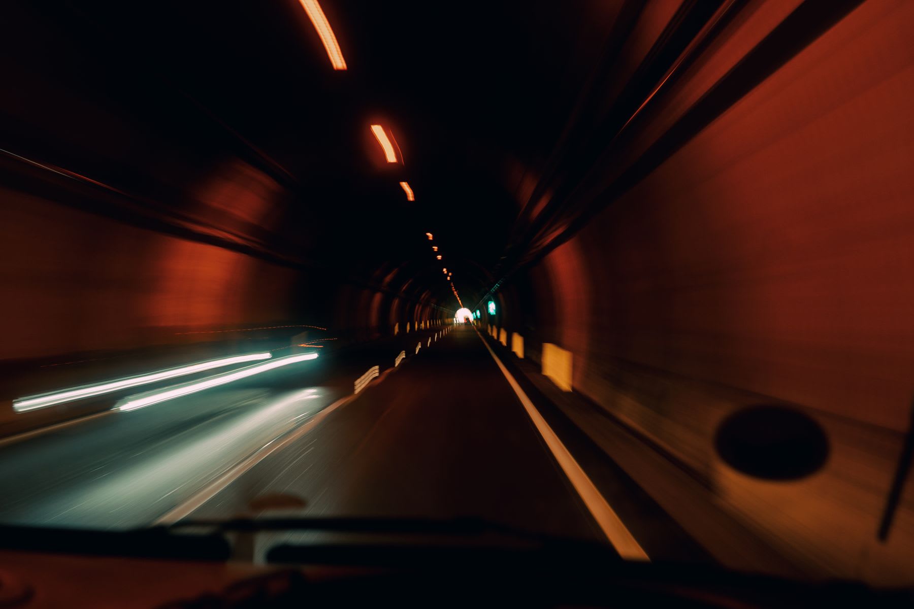 A motion-blurred, long-exposure shot from inside a car speeding through an orange-lit highway tunnel at night.