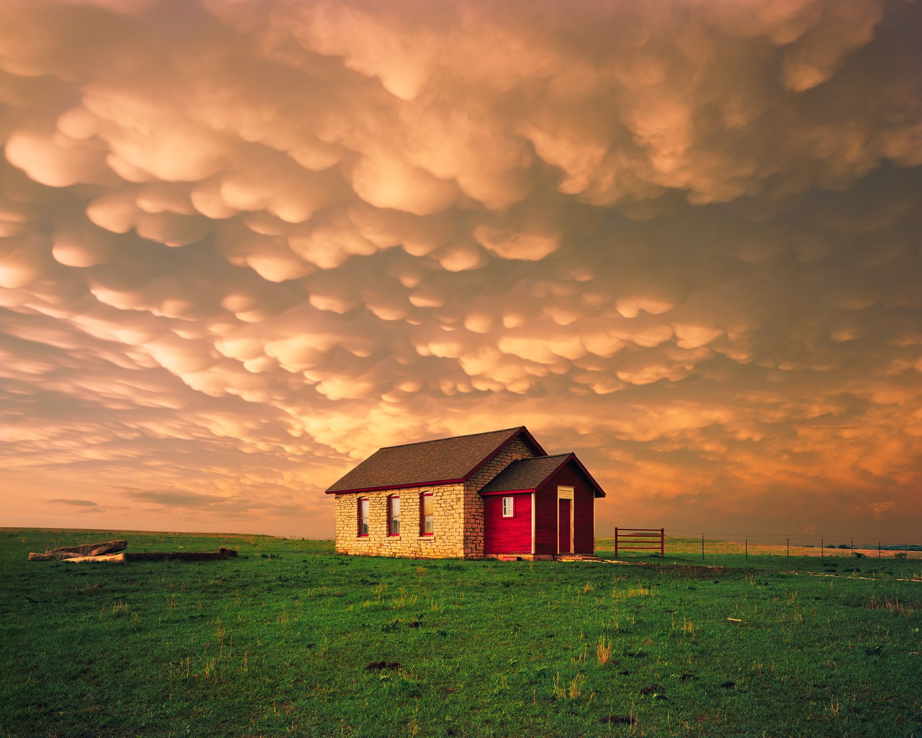 A small brick house in a green field under a dramatic sky with orange clouds.