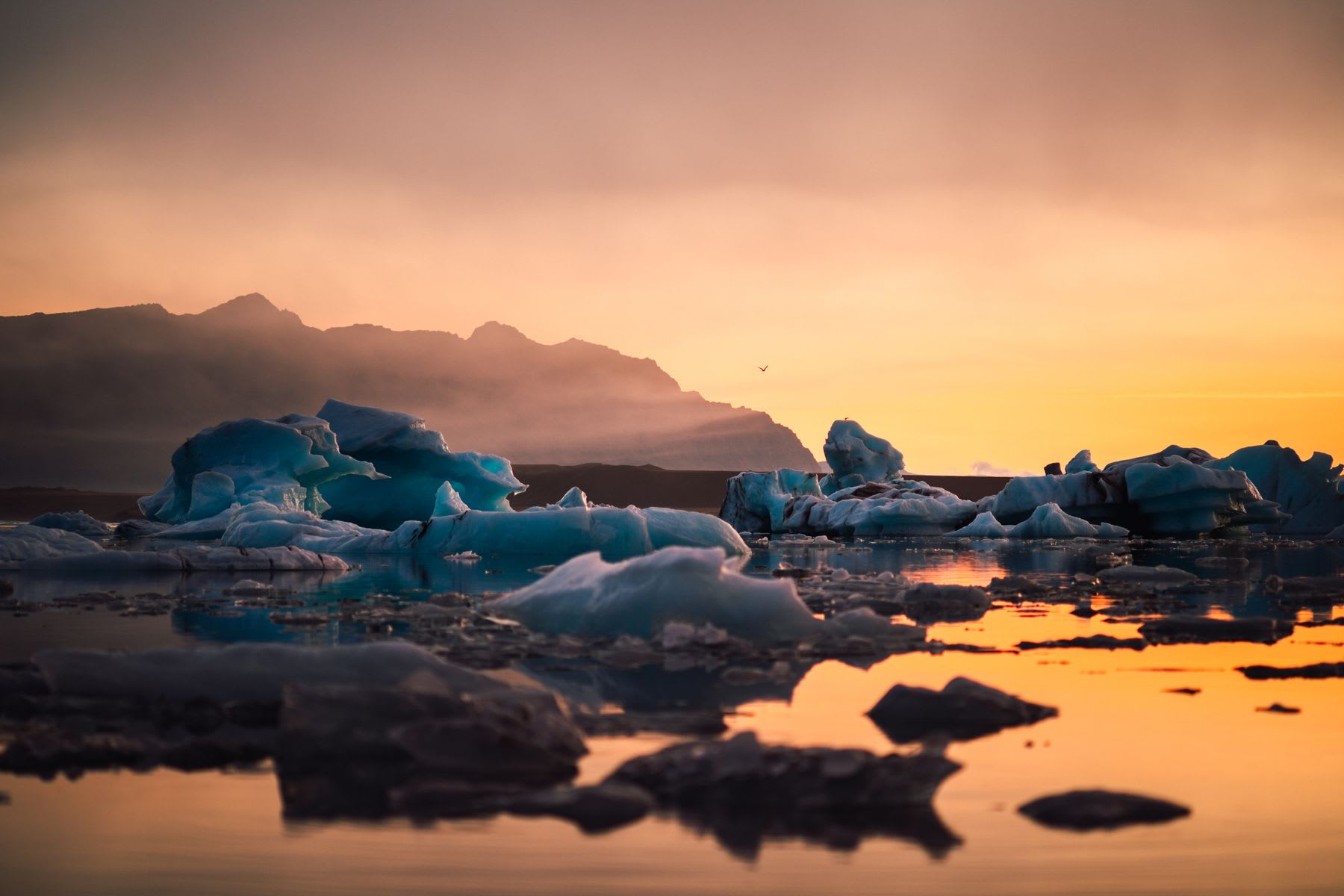A series of ice formations float on a puddle of water near a mountain at sunset on a cloudy day.
