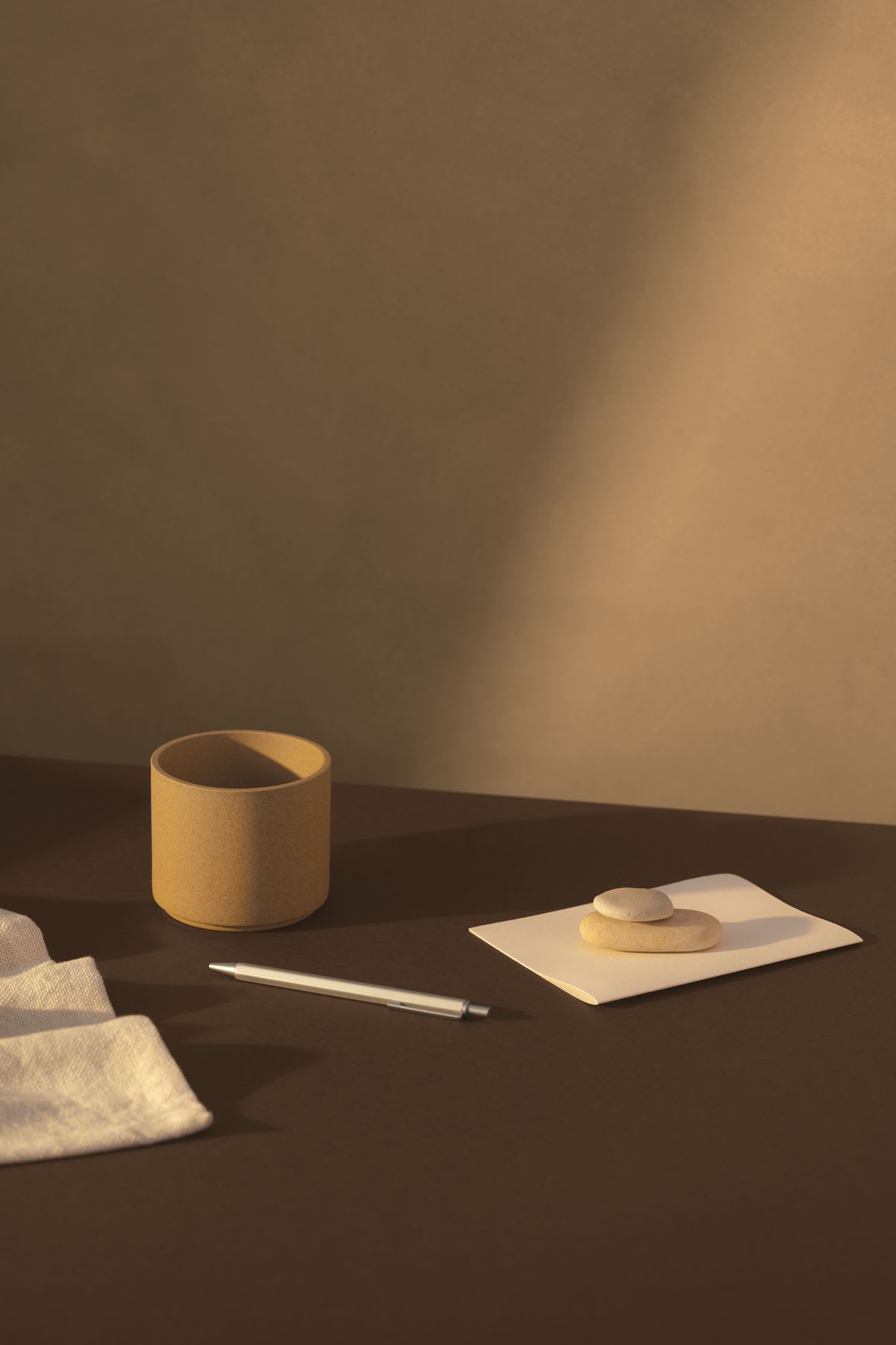 Simple glass, a napkin, an envelope with stones and a pen rest on a table illuminated by soft light.