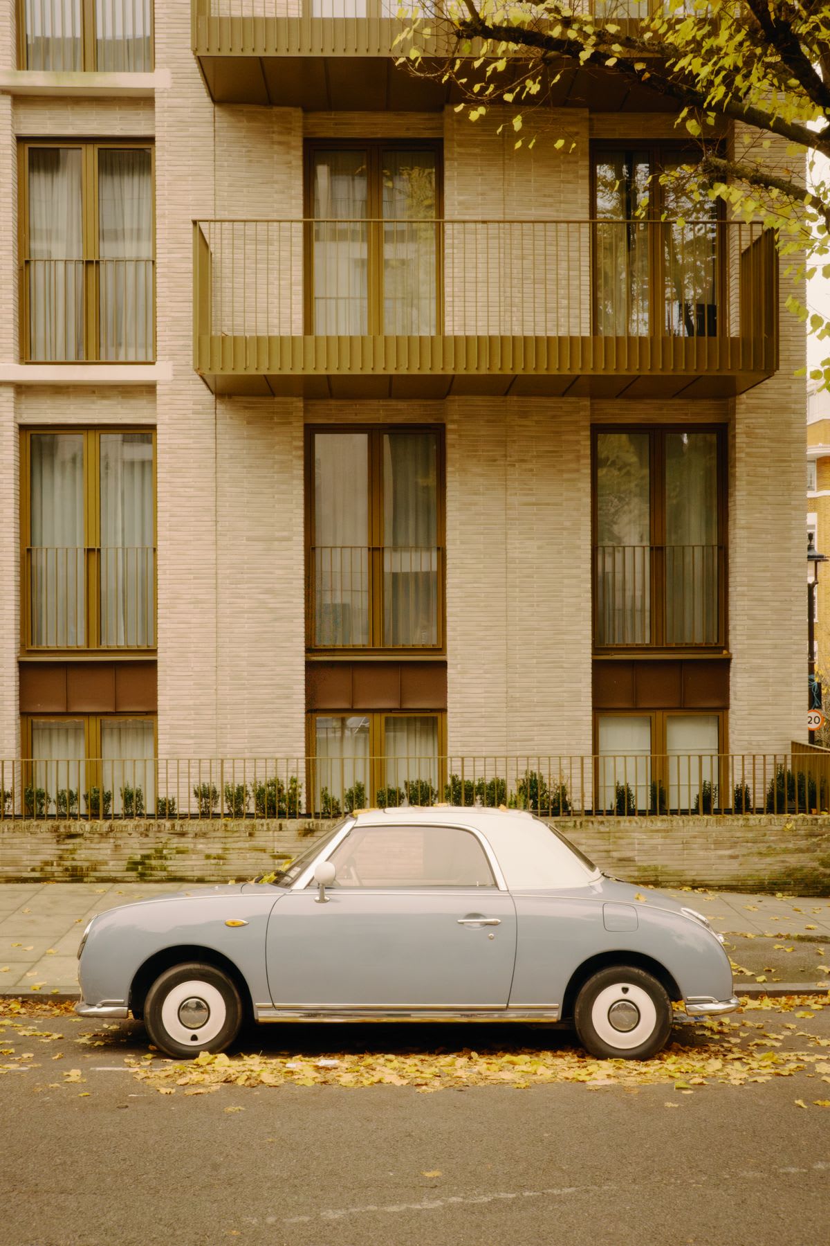 A small car parked on the street in front of a hotel or apartment buliding.