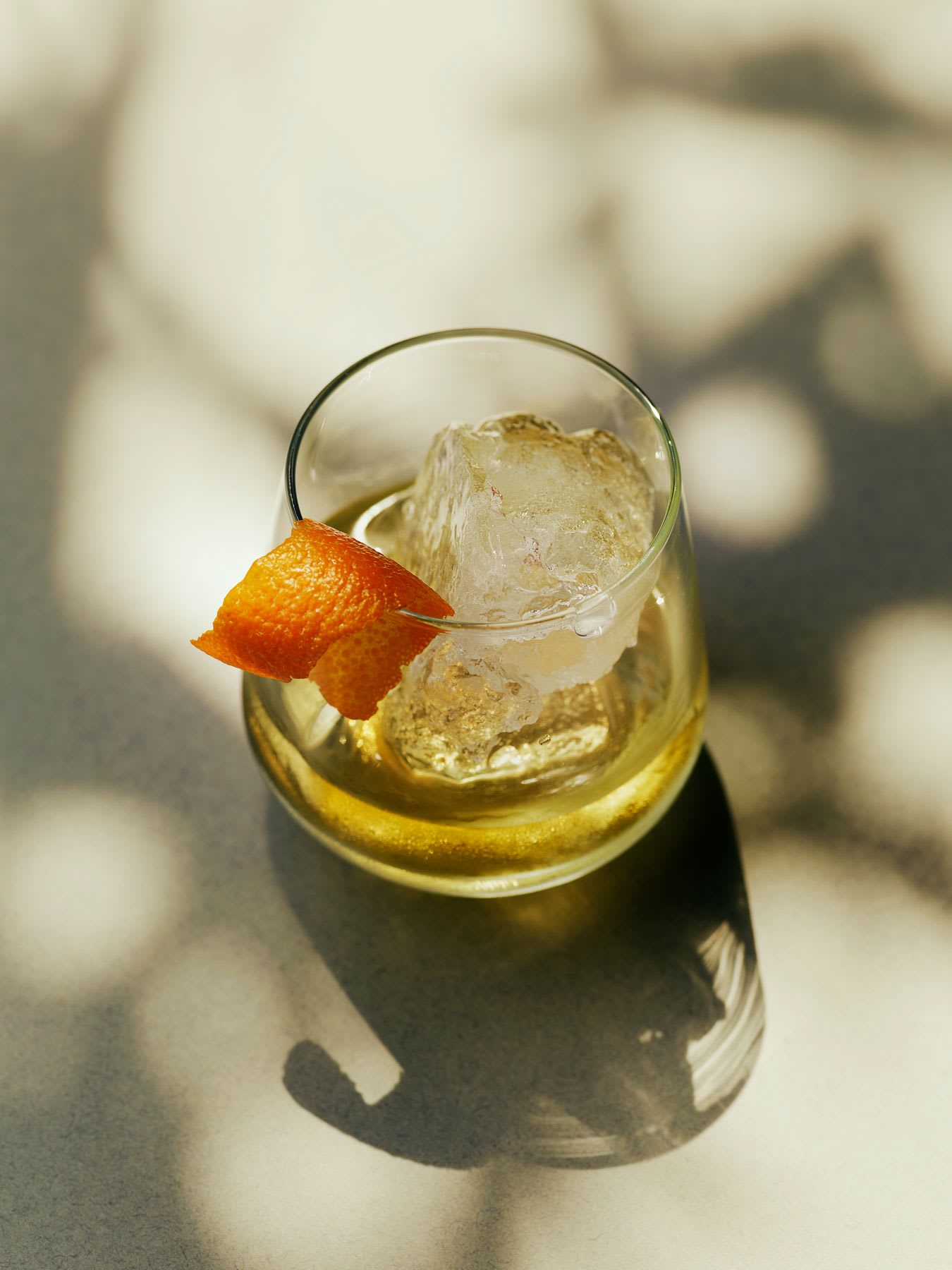 A glass of alcohol contains an orange peel garnish.