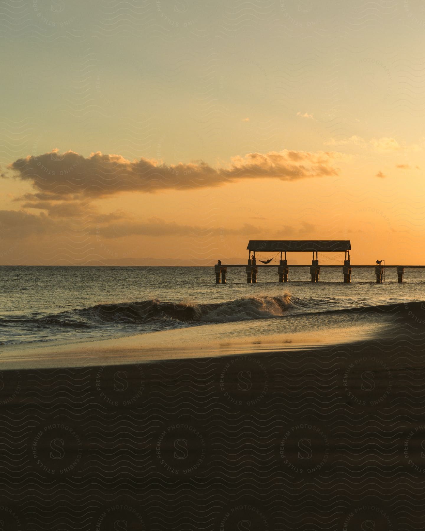 Waves roll into shore under the pier and over the beach at sunset