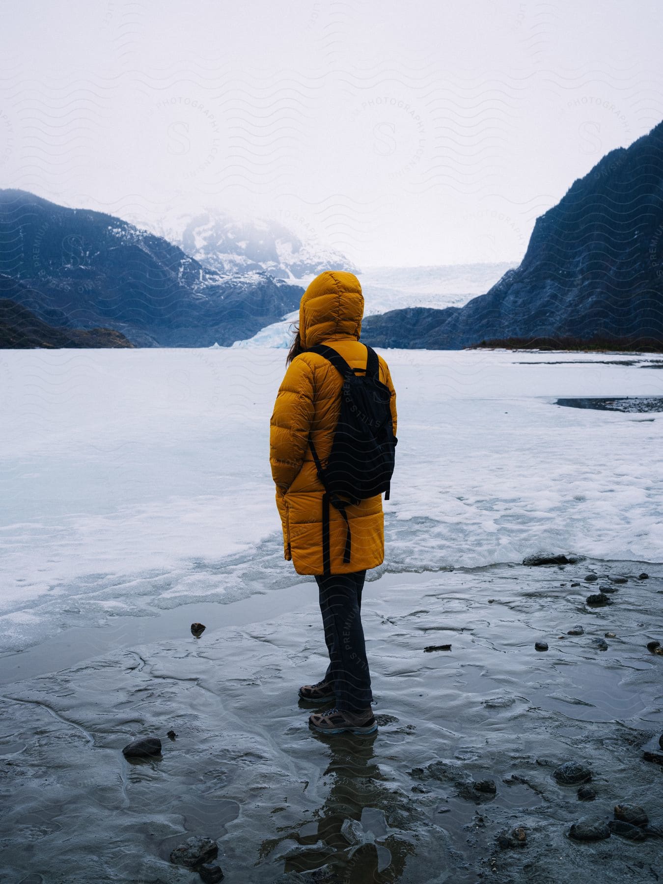 A woman wearing a yellow jacket looking out onto snow on a glacier.