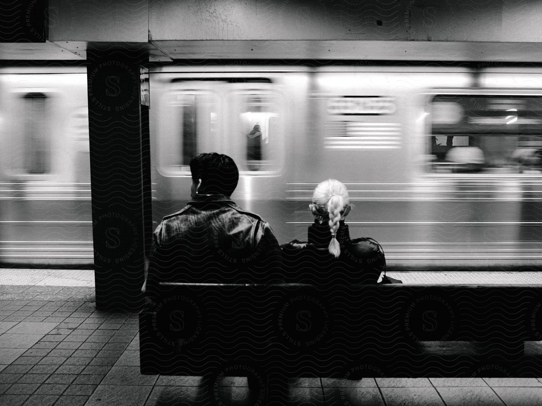 A man and woman sitting on a bench watching a subway train go by.