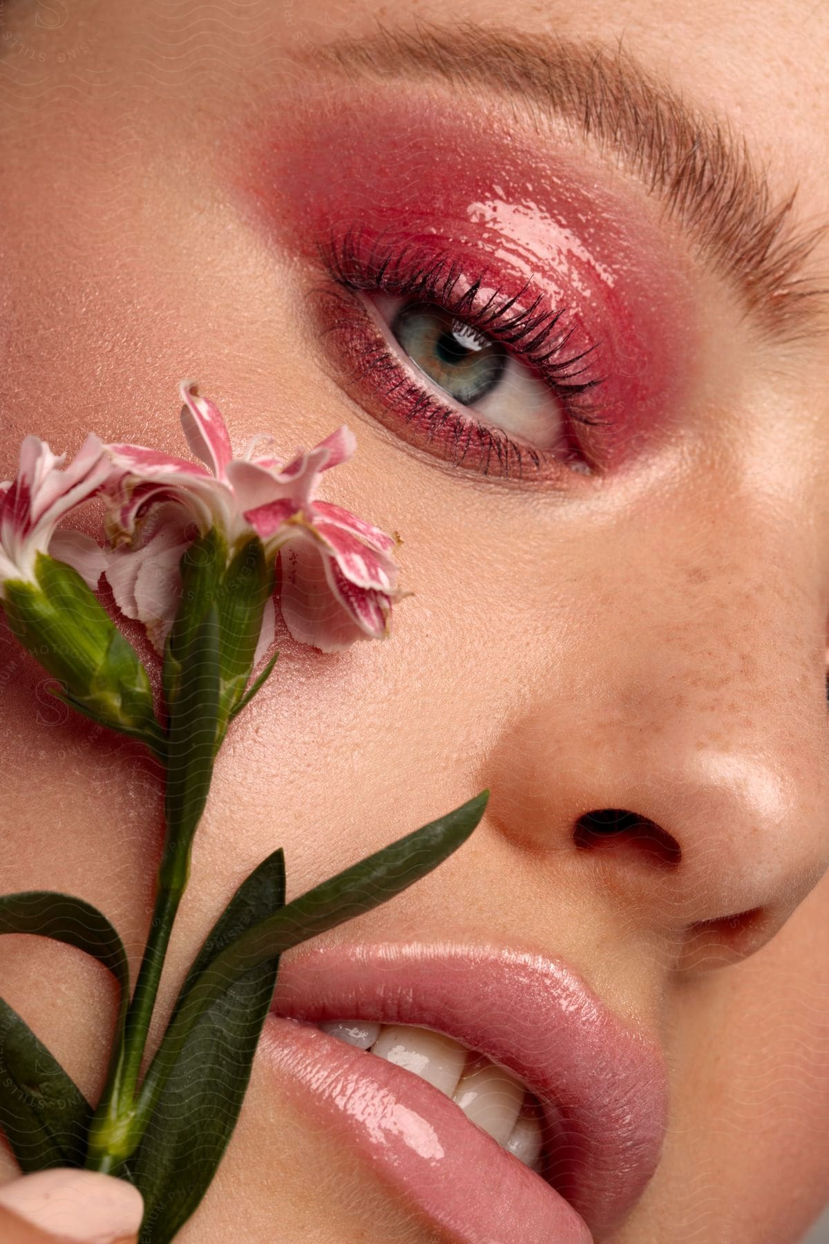 A woman placing a clove pink under her eye, complemented by pink eyeliner.