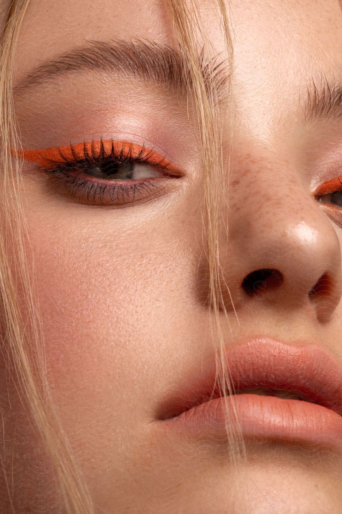 A blonde, teenage girl poses while wearing orange eyeliner.