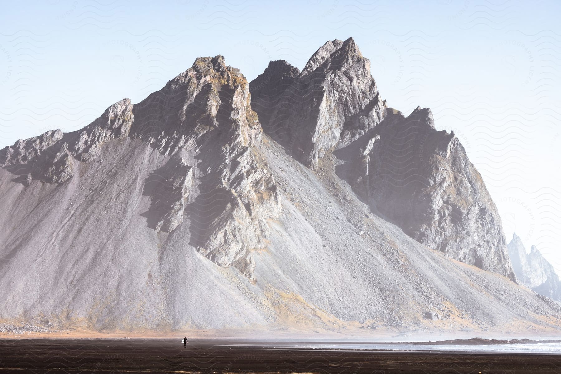 A person walks on a black sand beach in front of a majestic mountain.