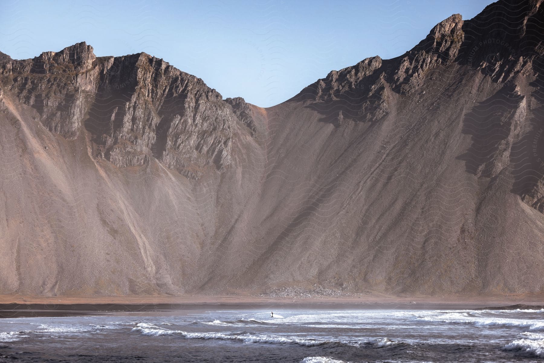 Waves roll onto beach near tall seaside cliff.