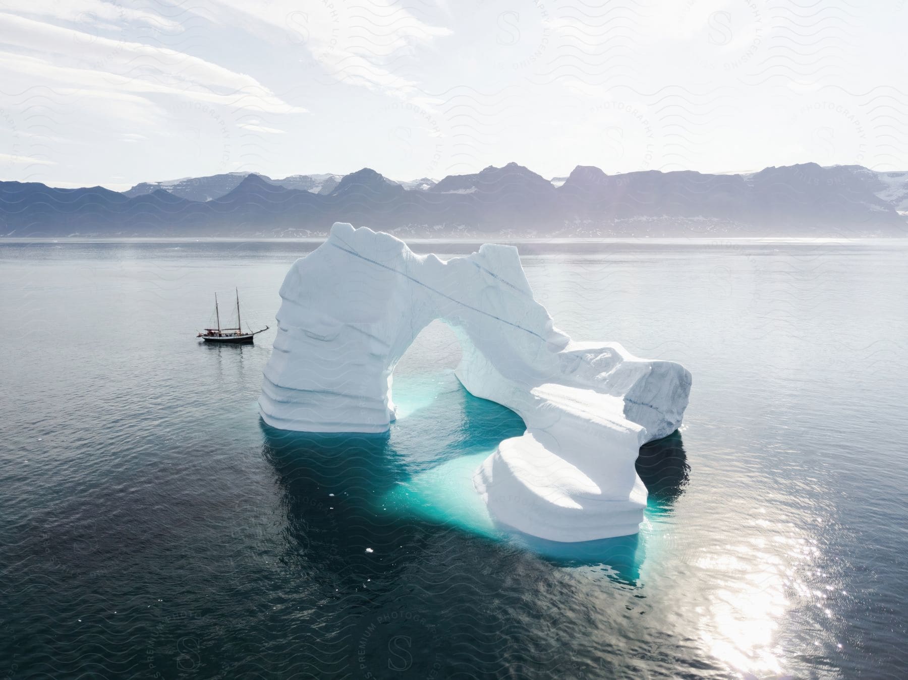 A sailboat is floating past a large ice structure in the water.