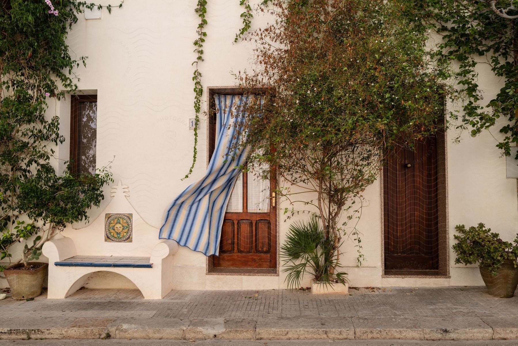 A blue and white striped curtain hangs from a door of a house, situated near a bench