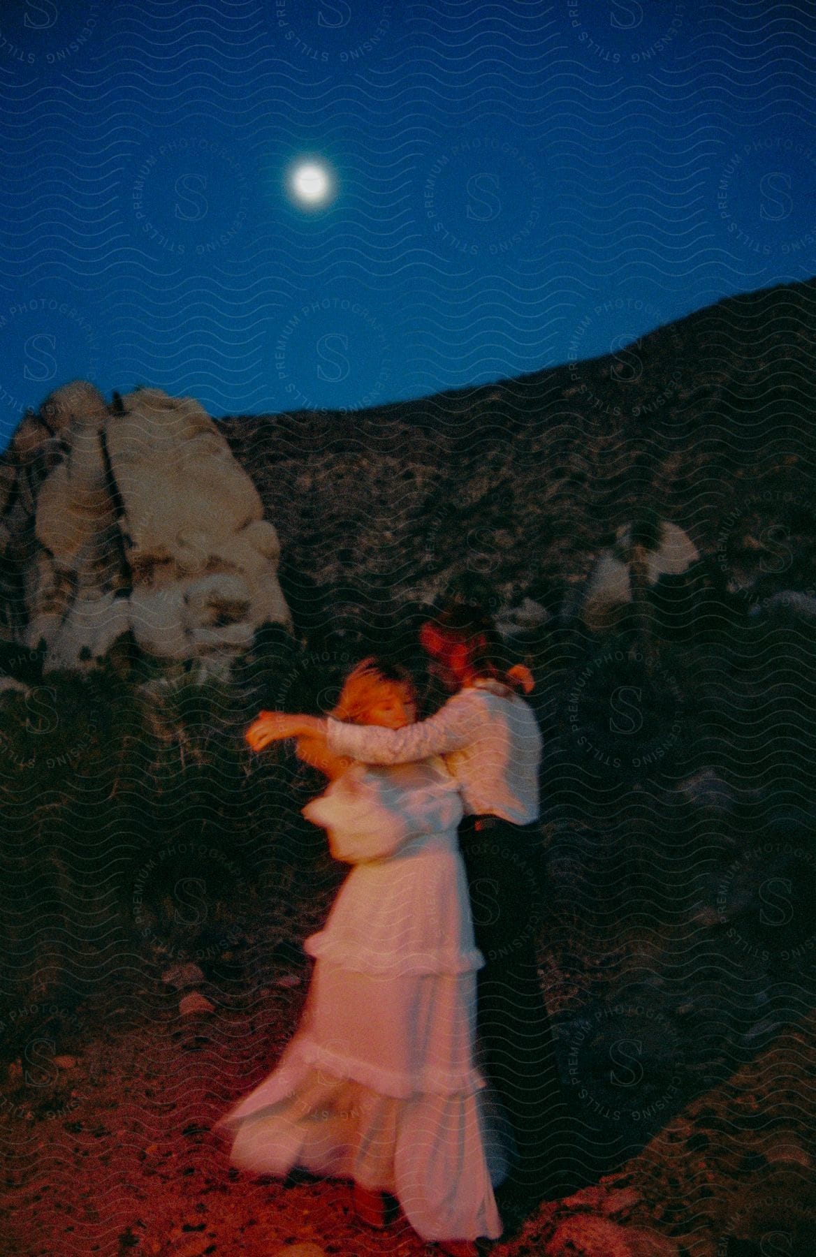 A man and a women are dancing outside under the moon.