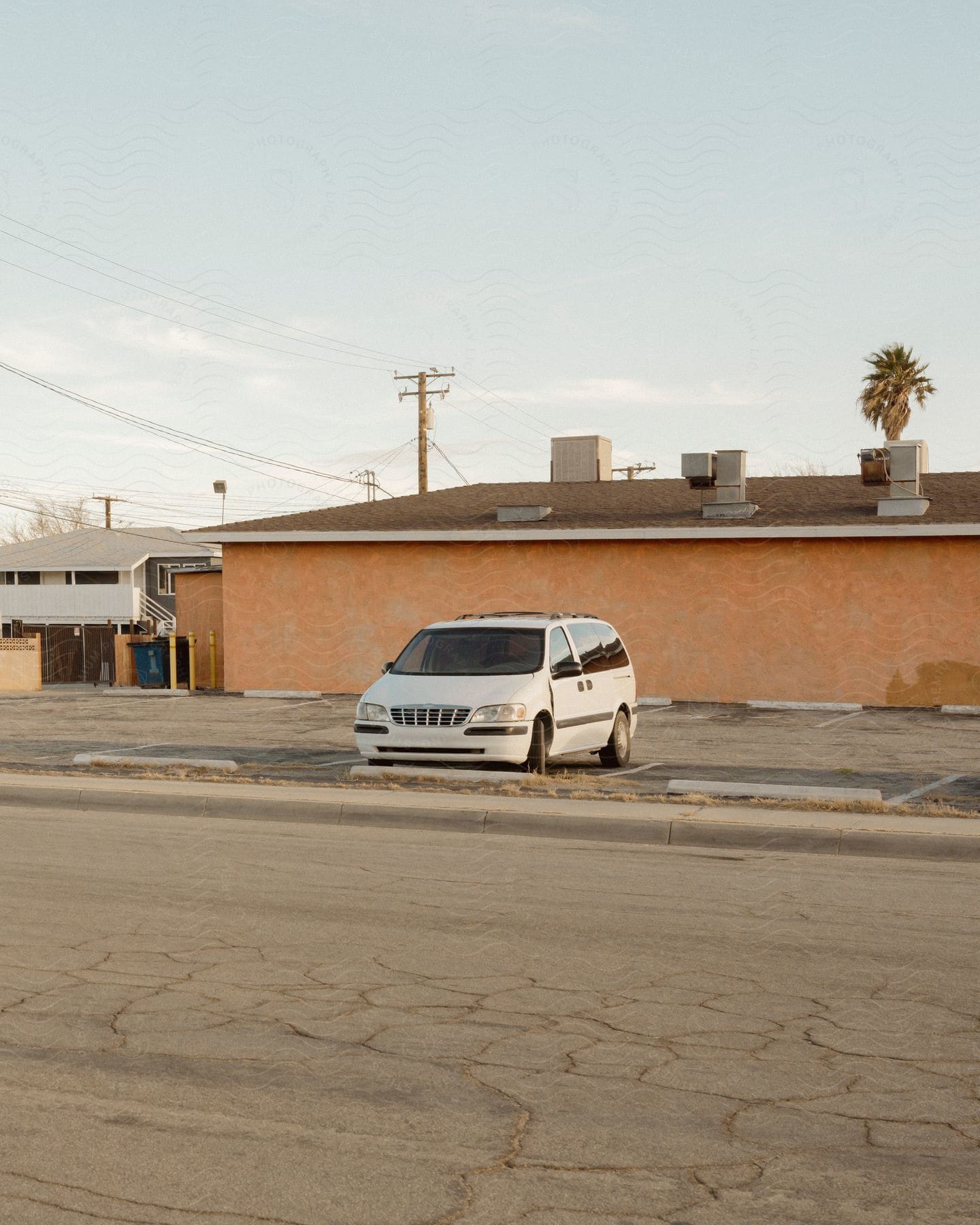 A white minivan parked in an empty sunlit parking lot