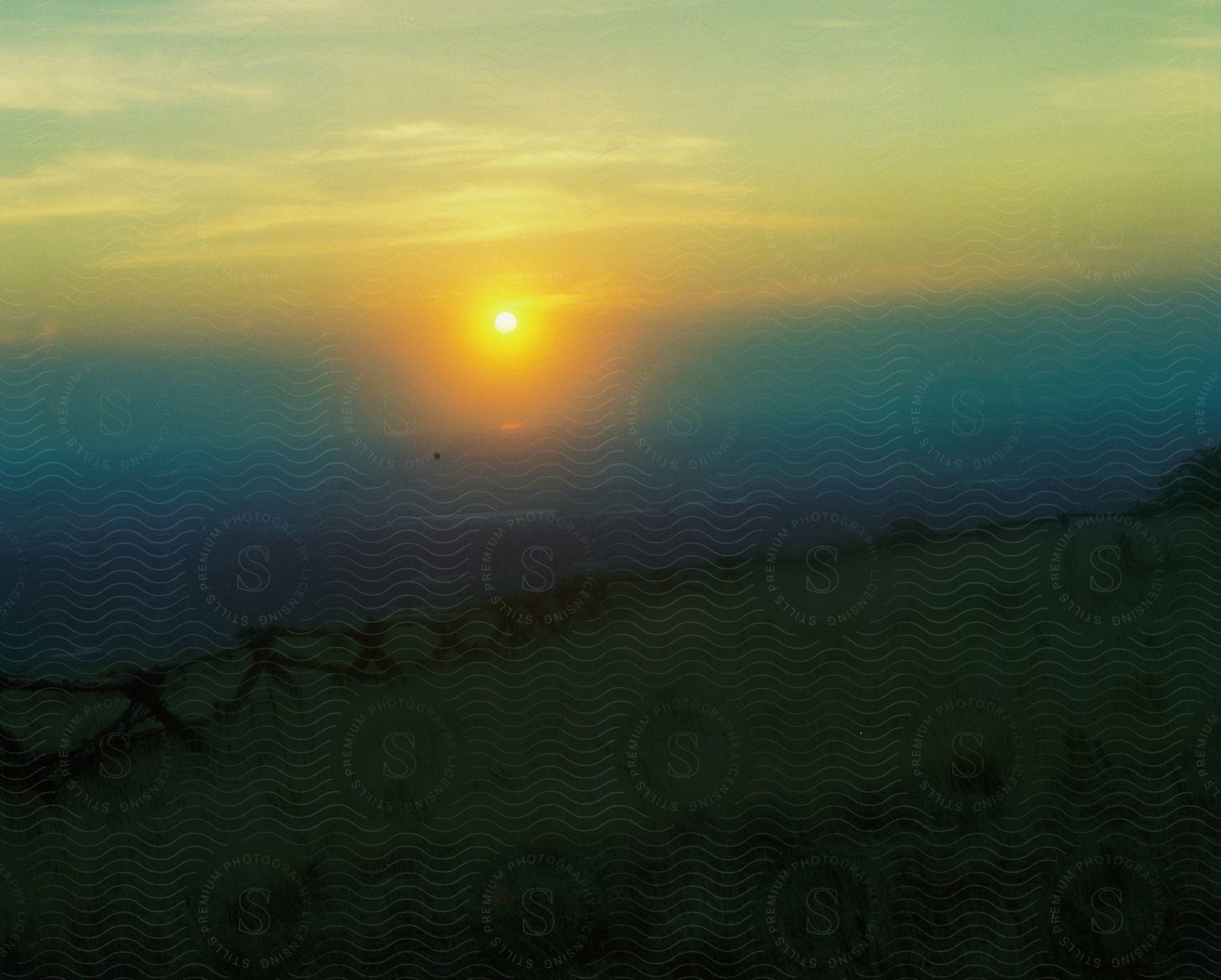 Stock photo of rising sun shines through dense fog onto fenced pasture.