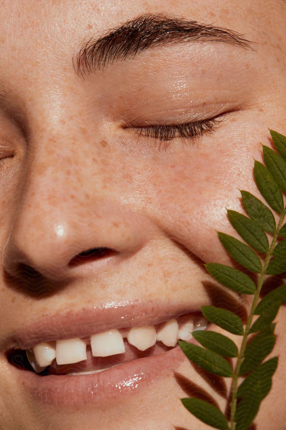 Close Up Of Freckled Face Of Smiling Woman Holding Plant Against Her Face