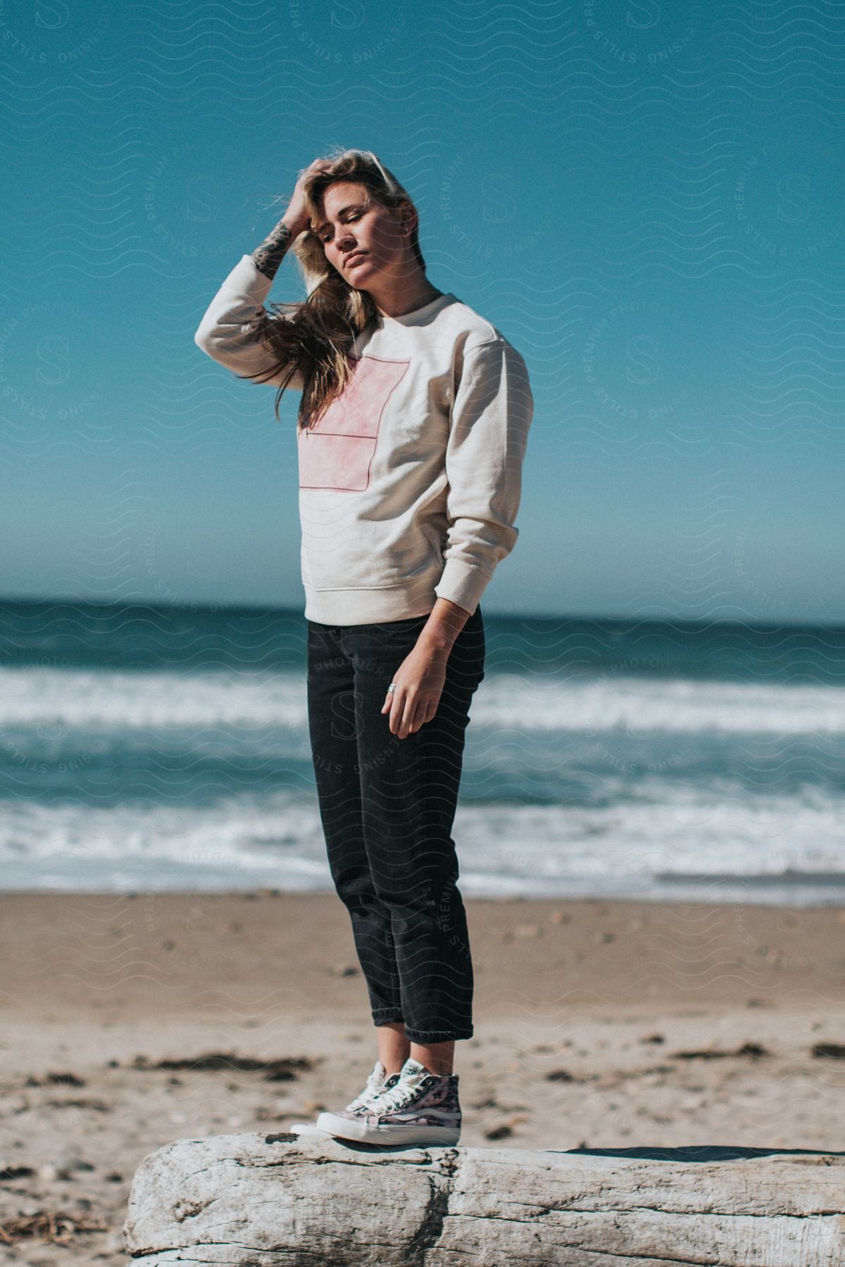 Woman on a wooden log at the beach posing with her hand on her head.