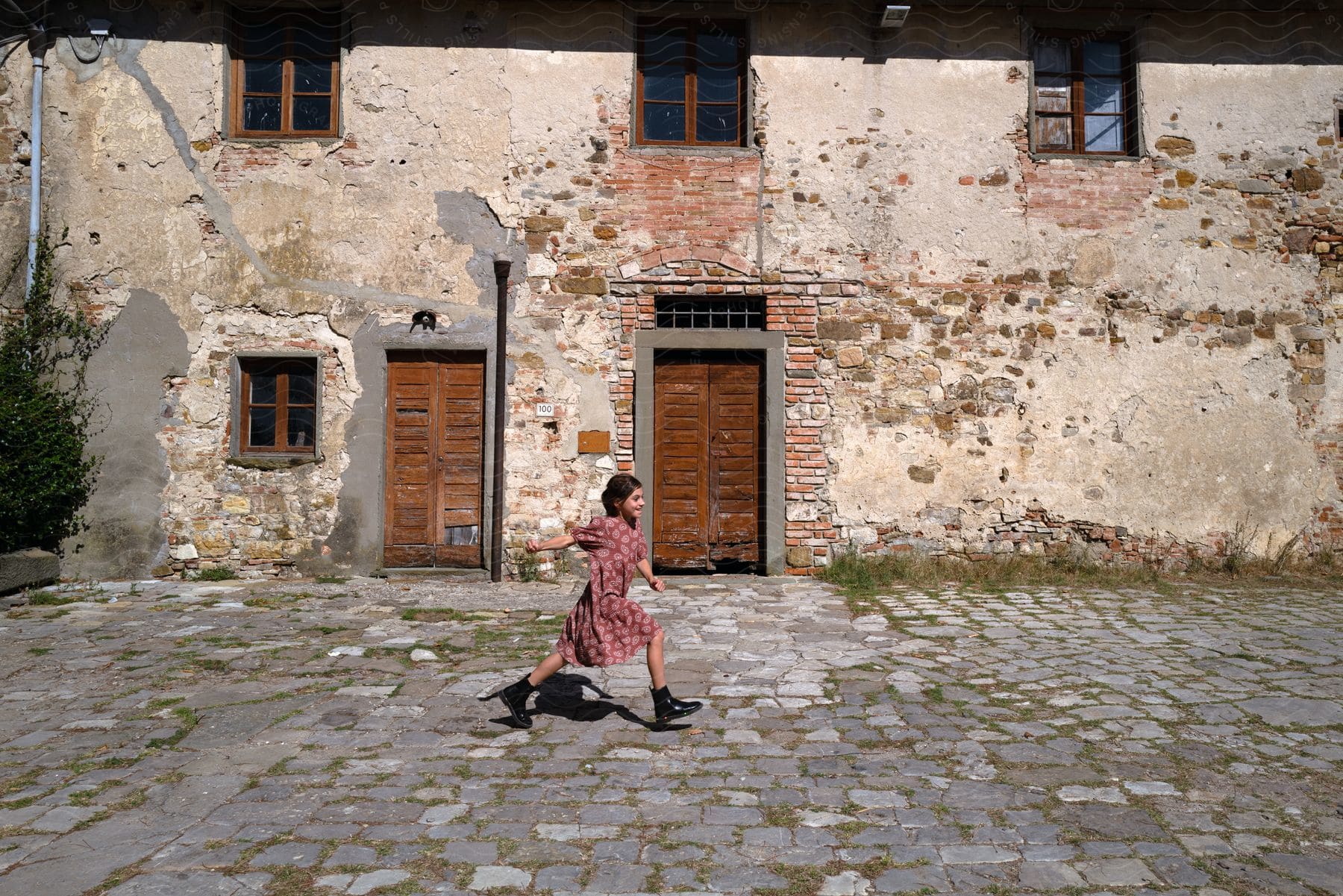 A child running in a flowered dress in front of an old building.