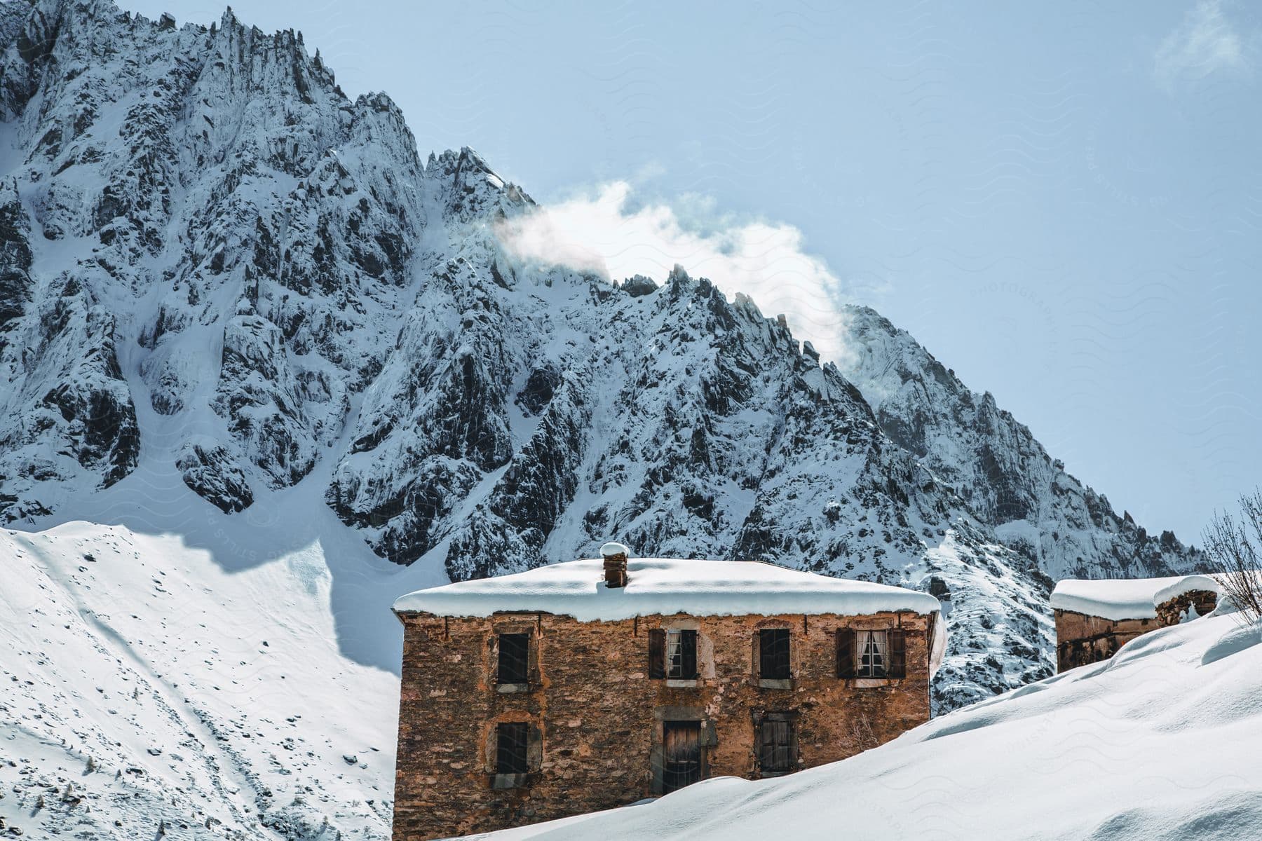 An old brick home is situated in front of a snow covered mountain.