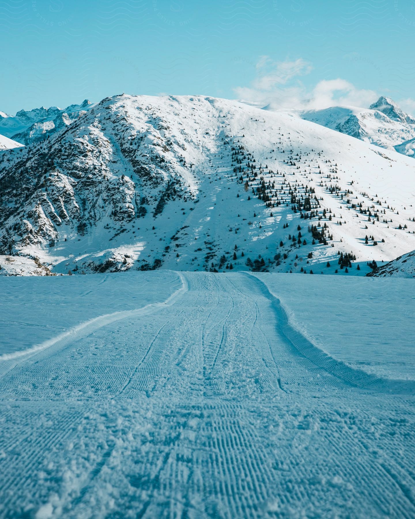 Vehicle tracks across a snow plain, leading towards a snow covered mountain.