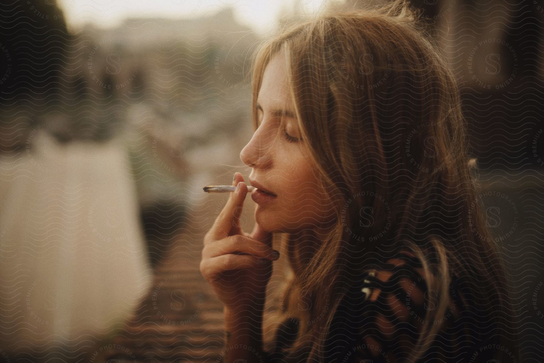female smokes a joint, in profile, outdoors