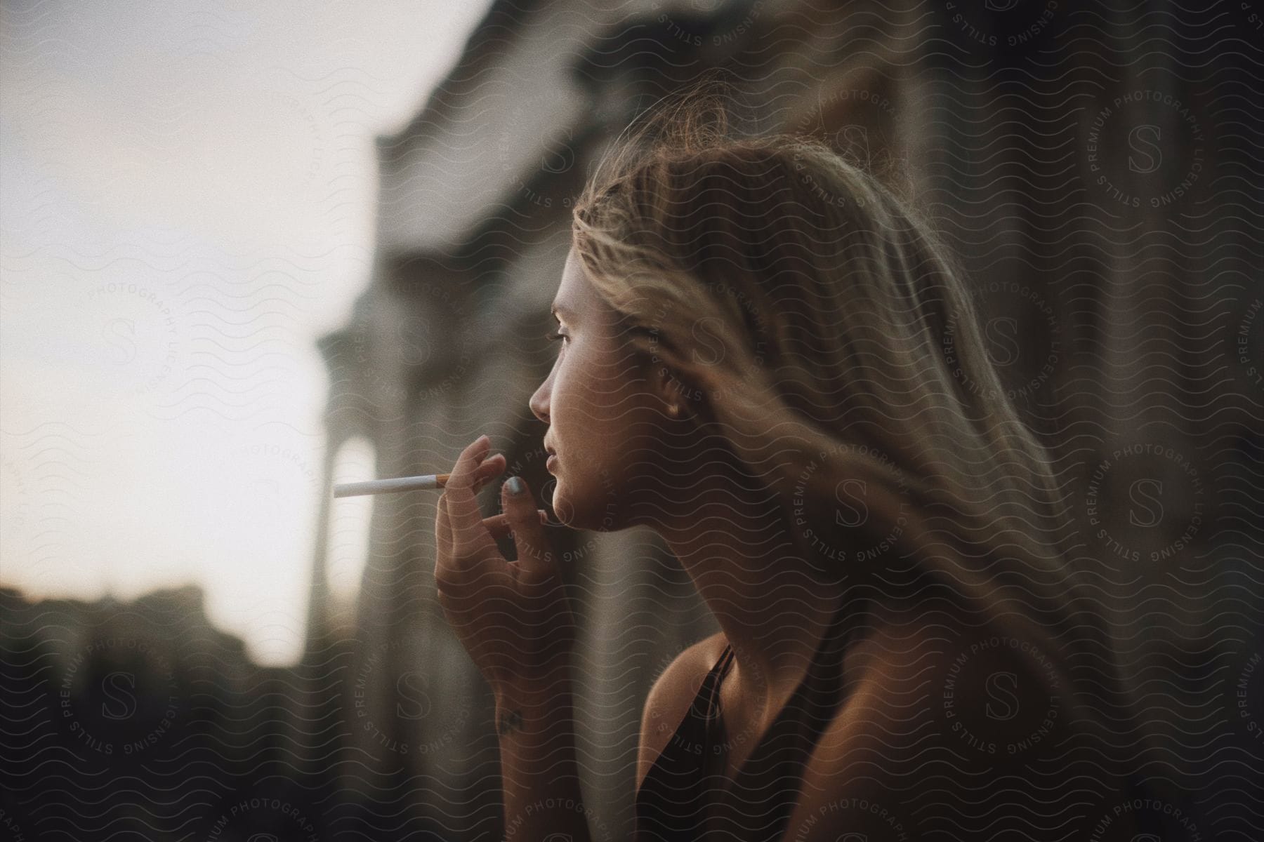 Young blonde woman smokes in the city at evening