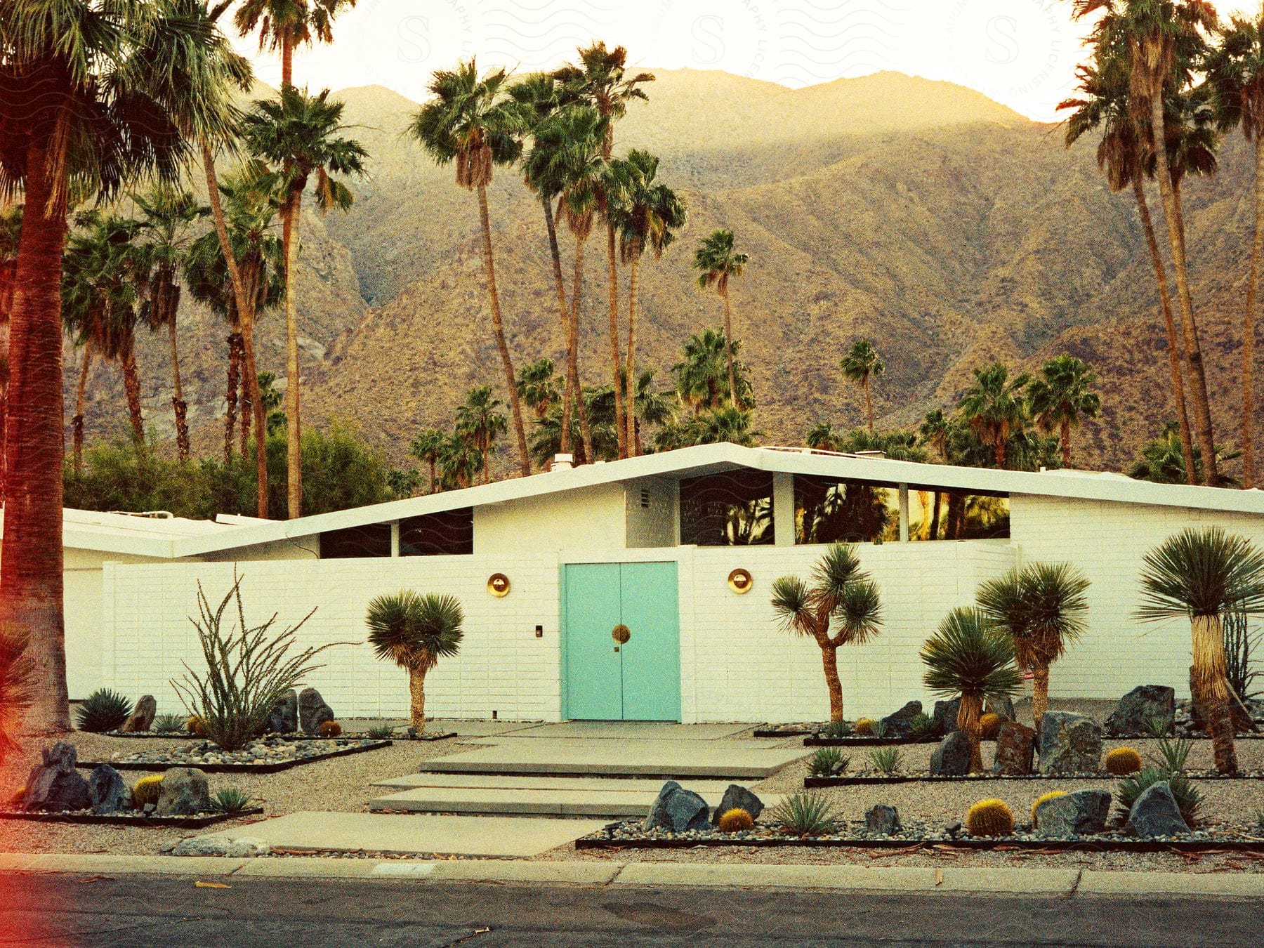 a house with a white brick wall and palm trees in front of a mountain range