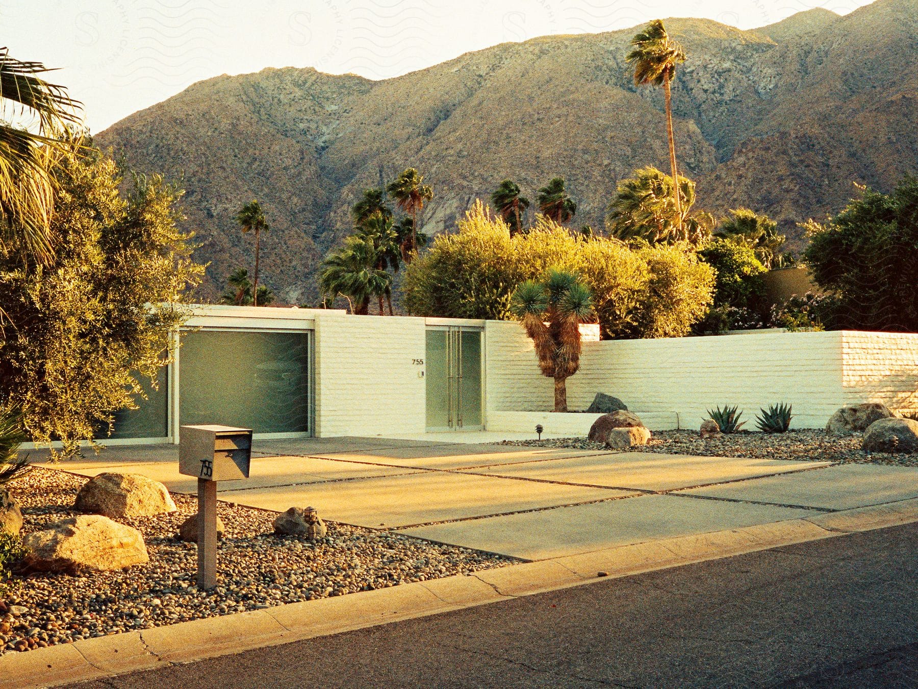 a house with a white brick wall and palm trees in front of a mountain range.
