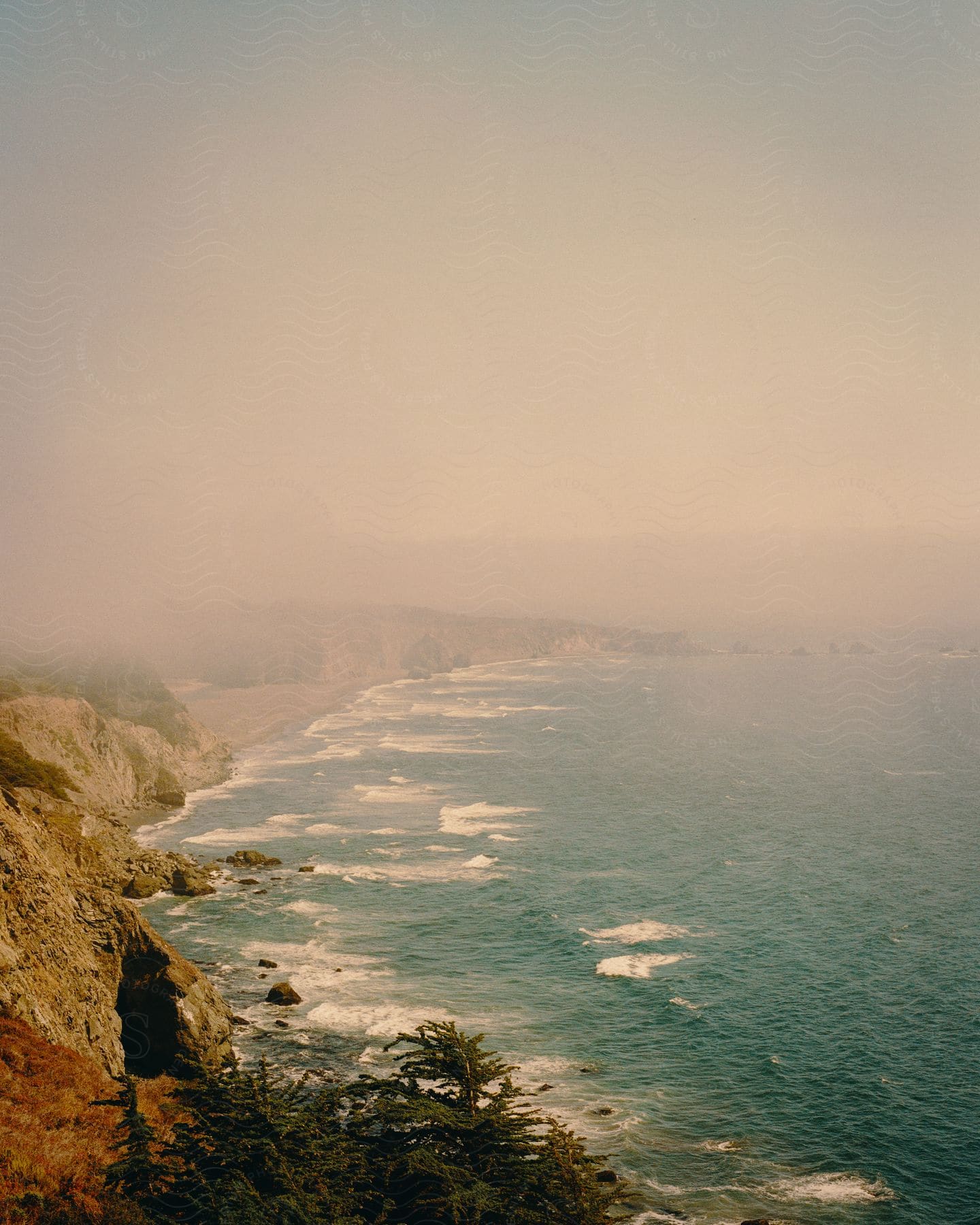 Aerial of mountainous coast with blue sea and fog.