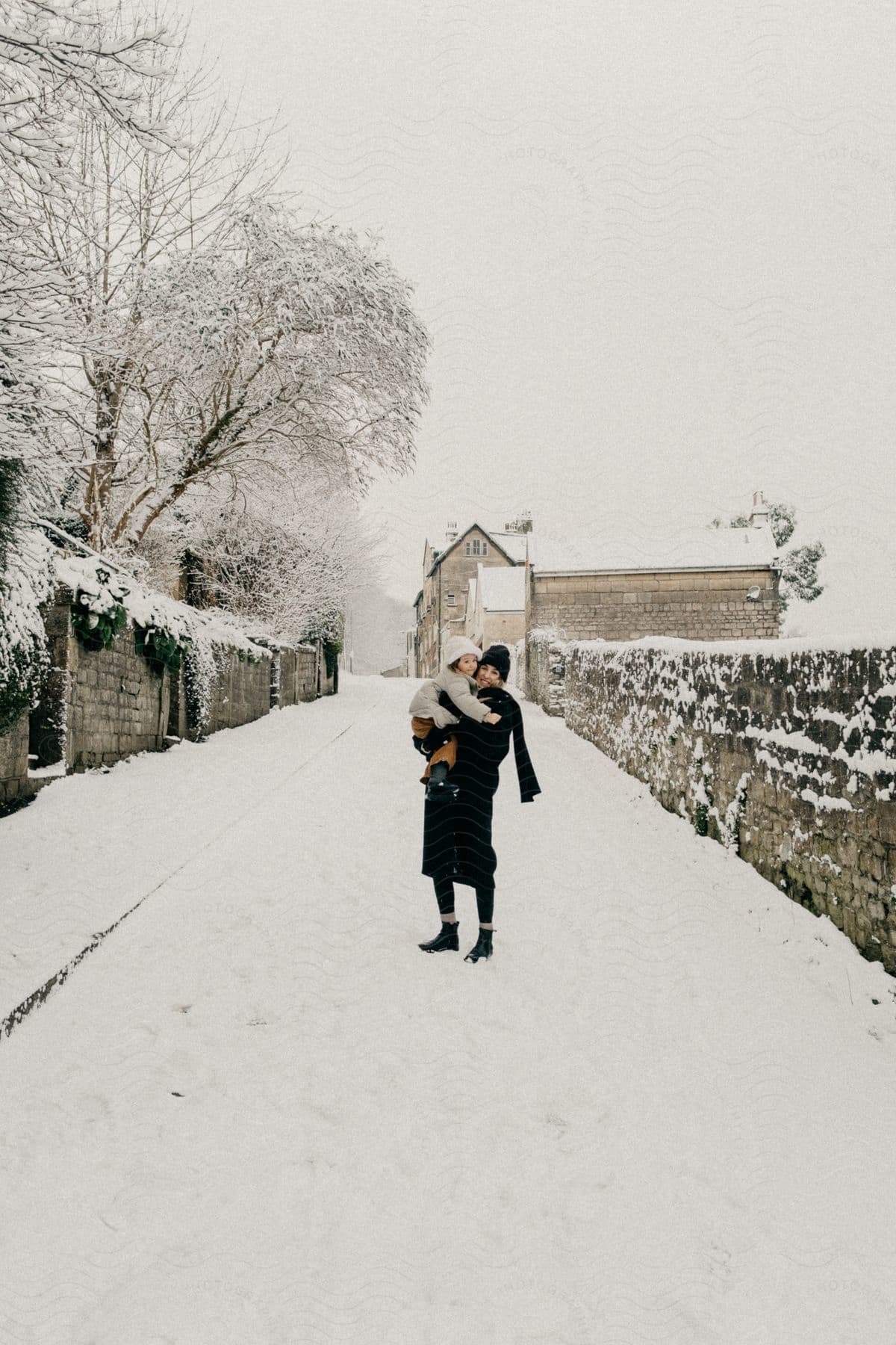 Mother with her daughter in her arms posing on a snow-covered village street.